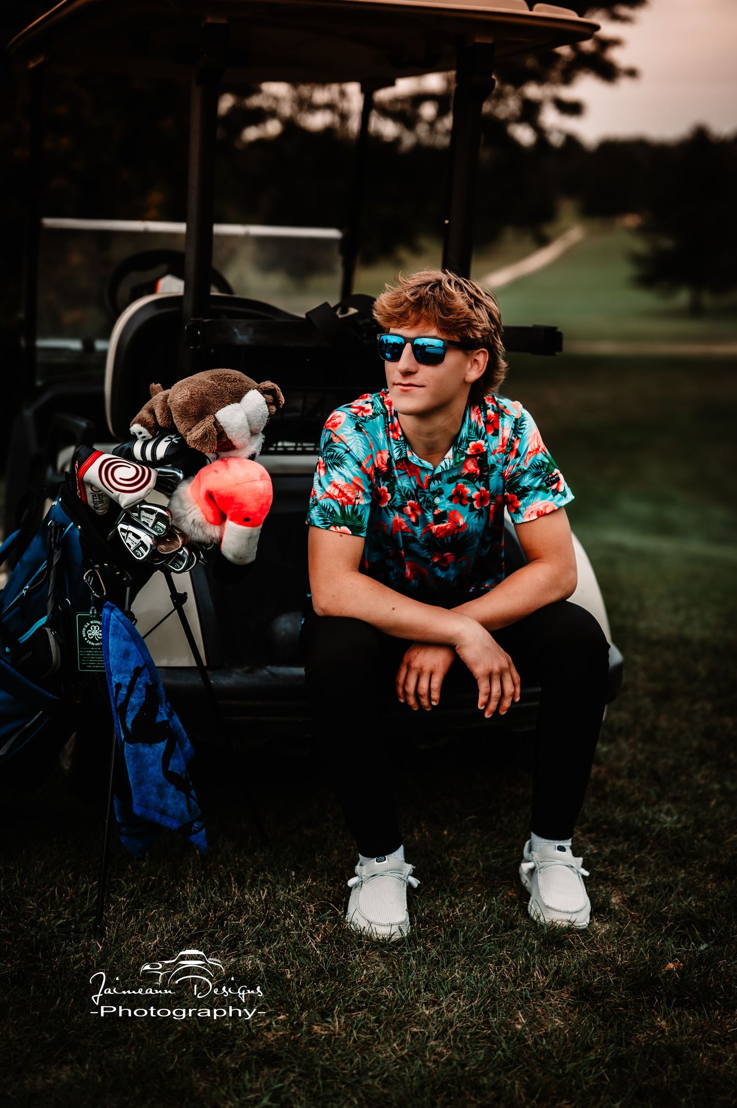 Golfer sitting on golf cart wearing tropical shirt and sunglasses at dusk.