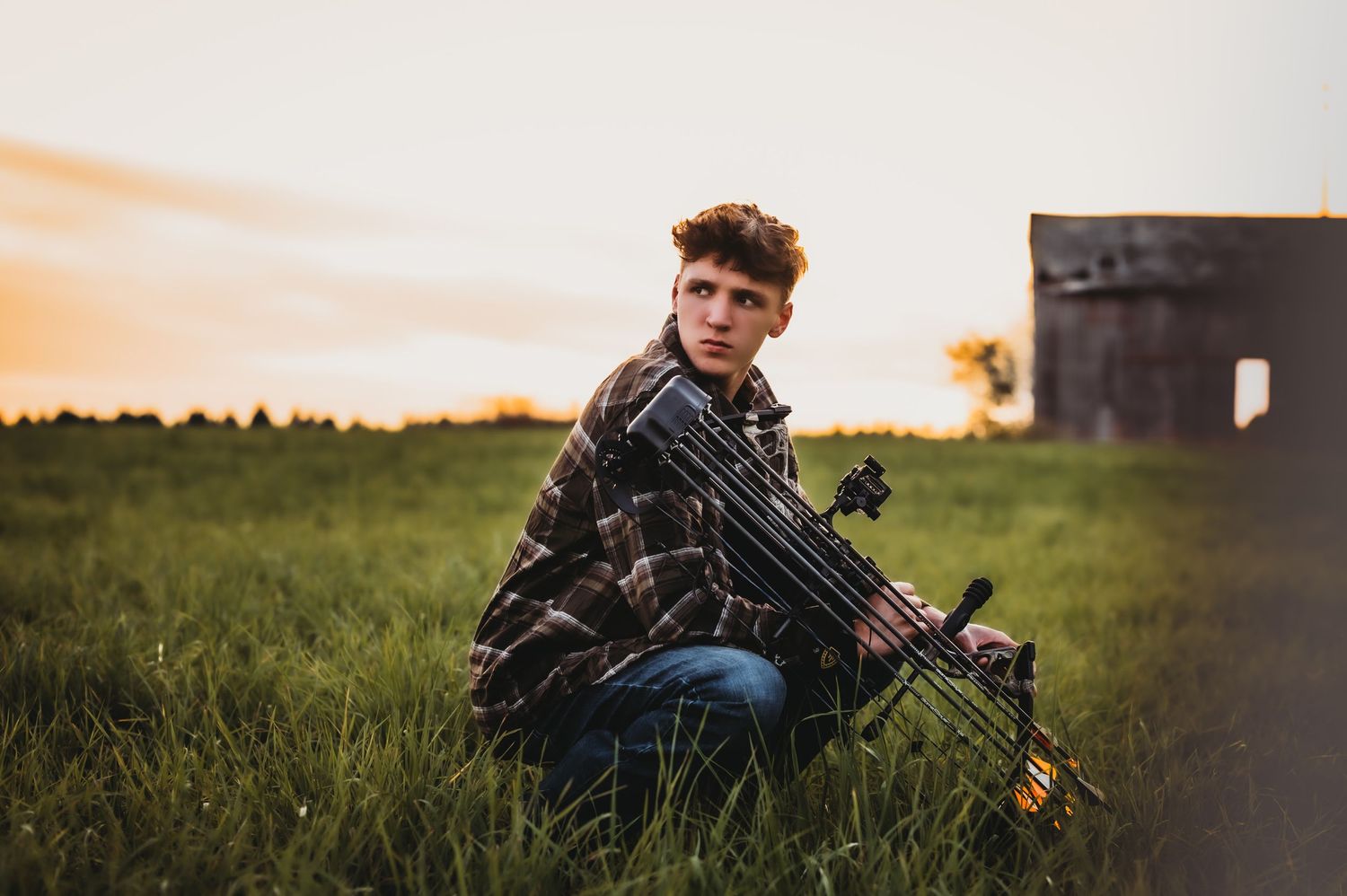 Sunset silhouette of person with tactical gear in grassy field.