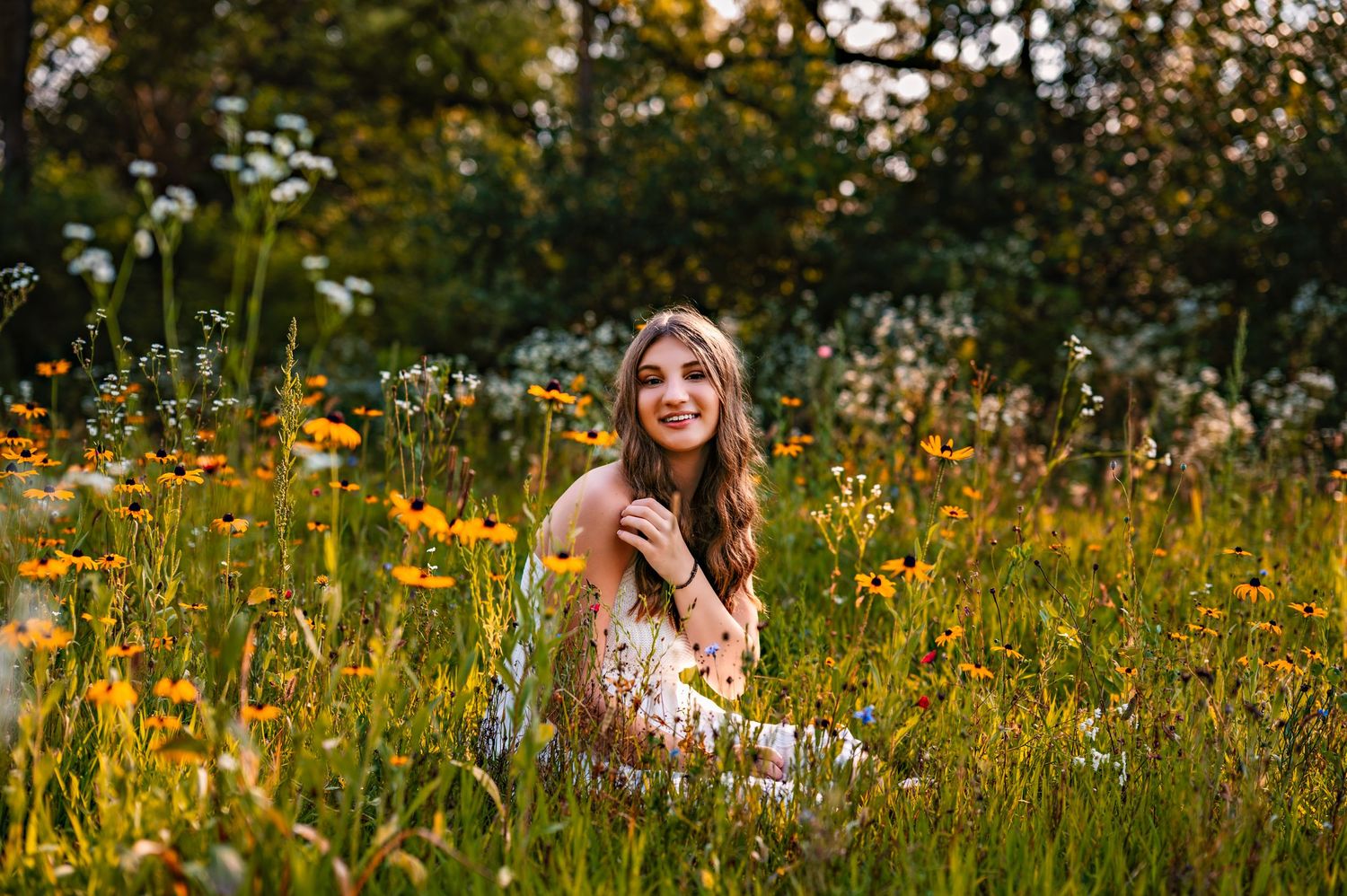 A joyful figure in a white dress sits among vibrant yellow wildflowers in a sunlit meadow during golden hour.