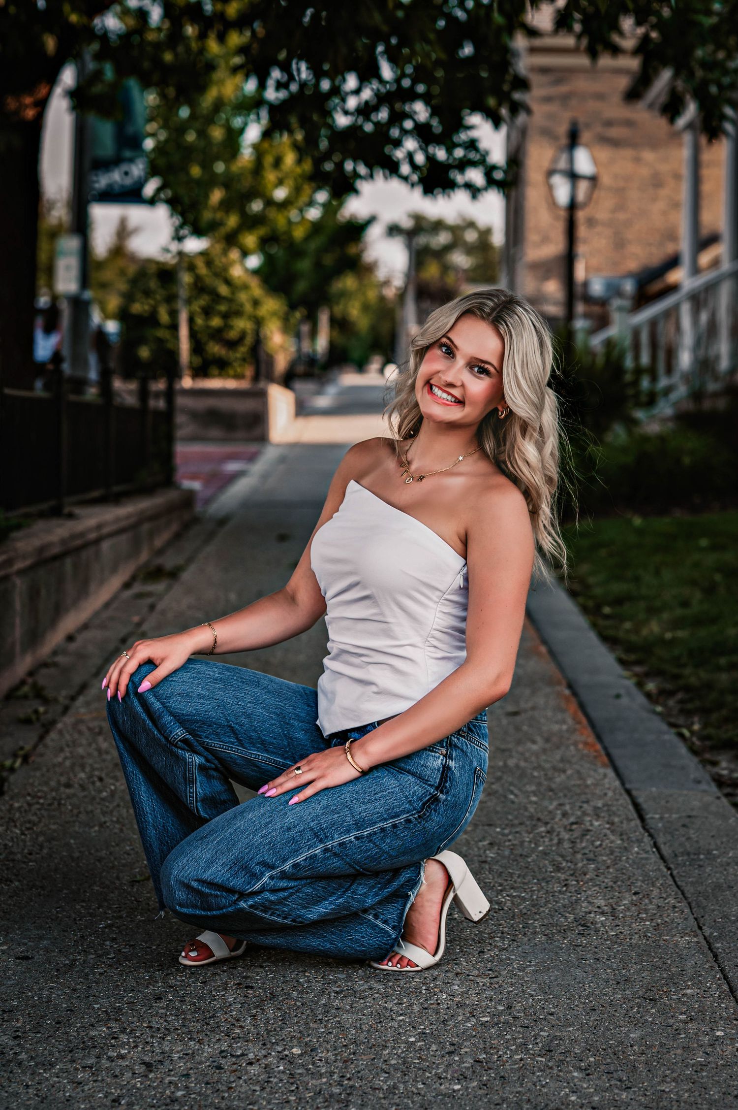 A person in a white top and blue jeans poses casually on an urban sidewalk during golden hour in Delafield, WI