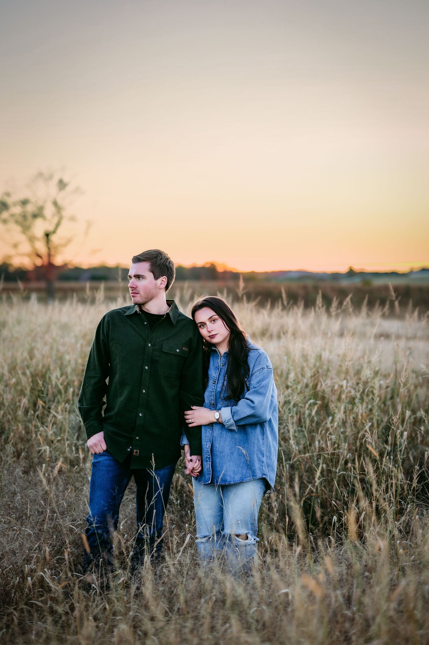 Couple laughing together in tall grass field during golden hour photo session.