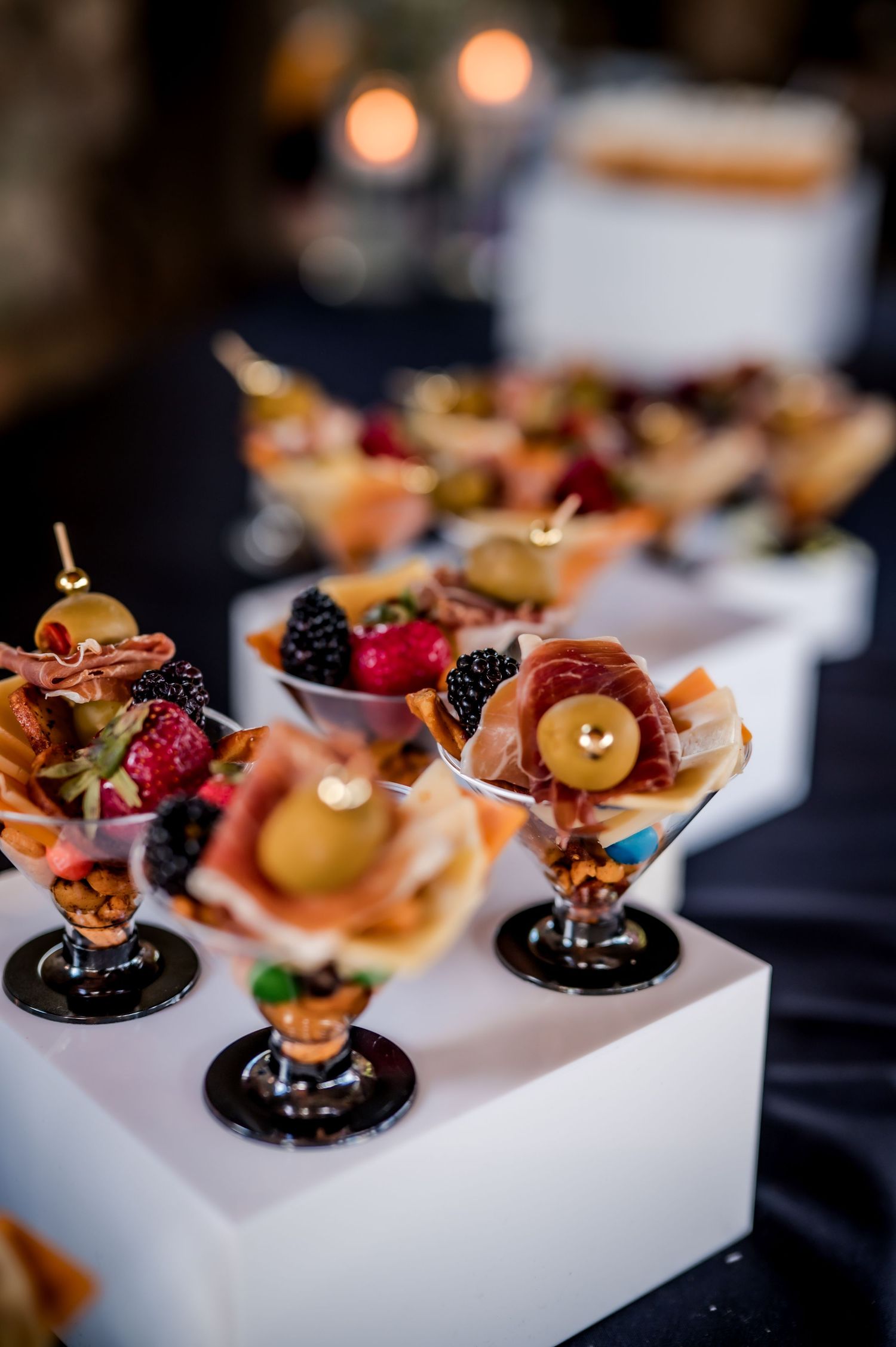 Elegant catering appetizers with fresh berries and garnishes served on modern white platforms at an upscale event.