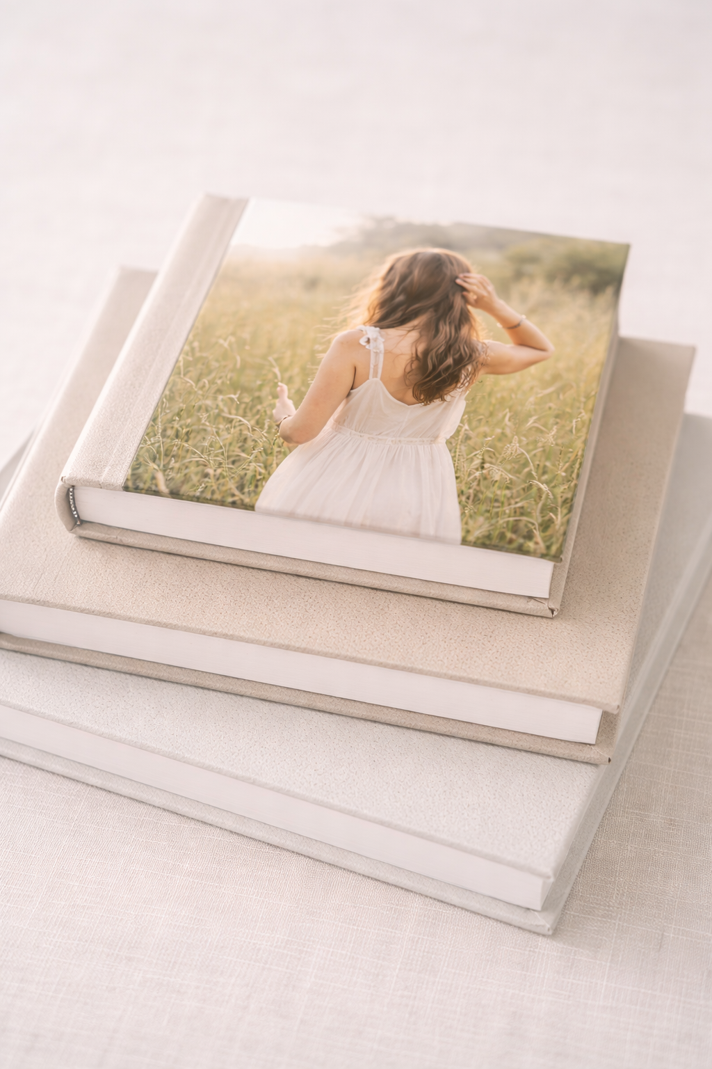 Stack of linen photo books with top book featuring a young girl in white dress standing in a golden field.