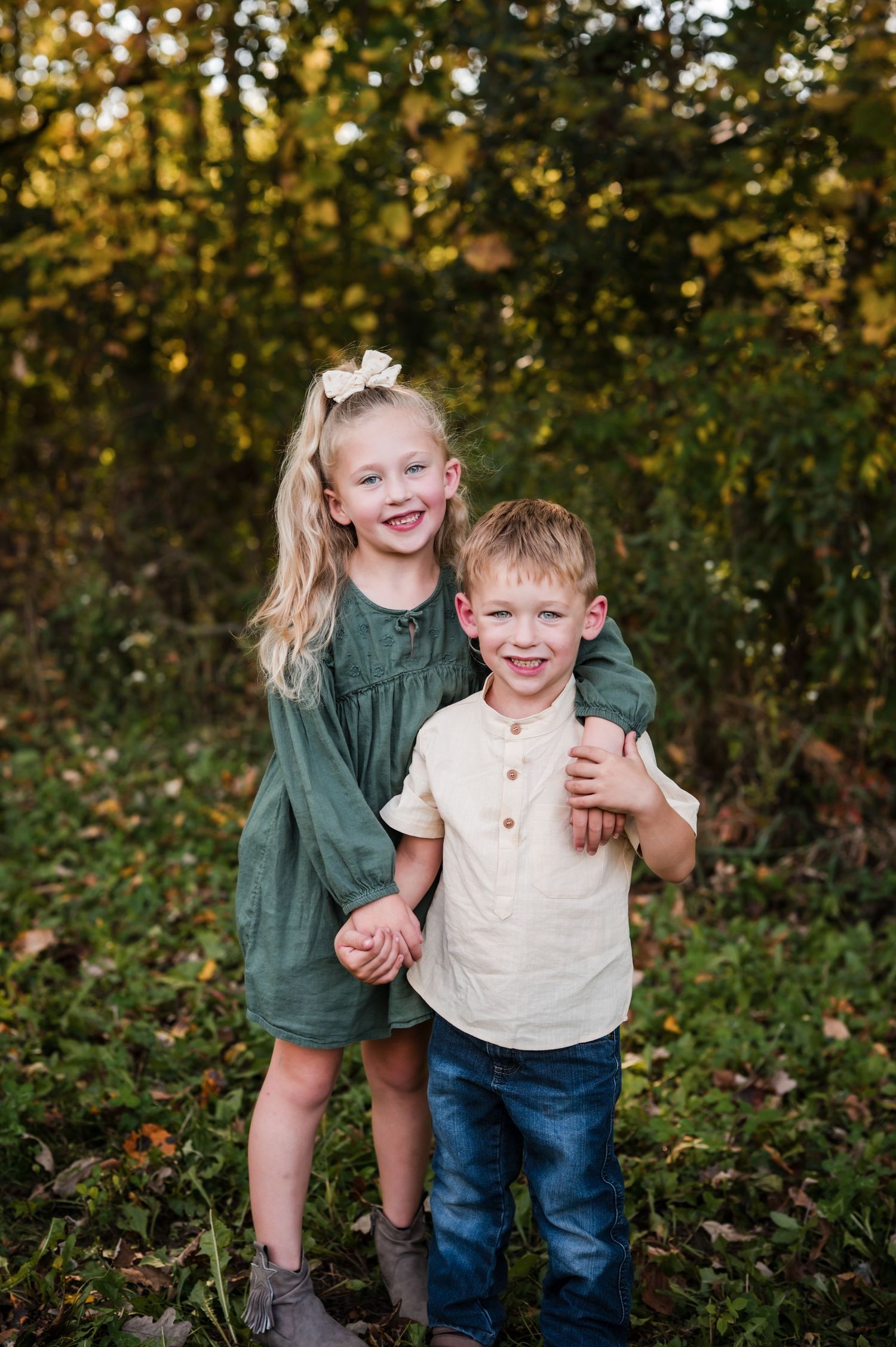 Two children playing and laughing together in a wooded outdoor setting during autumn.