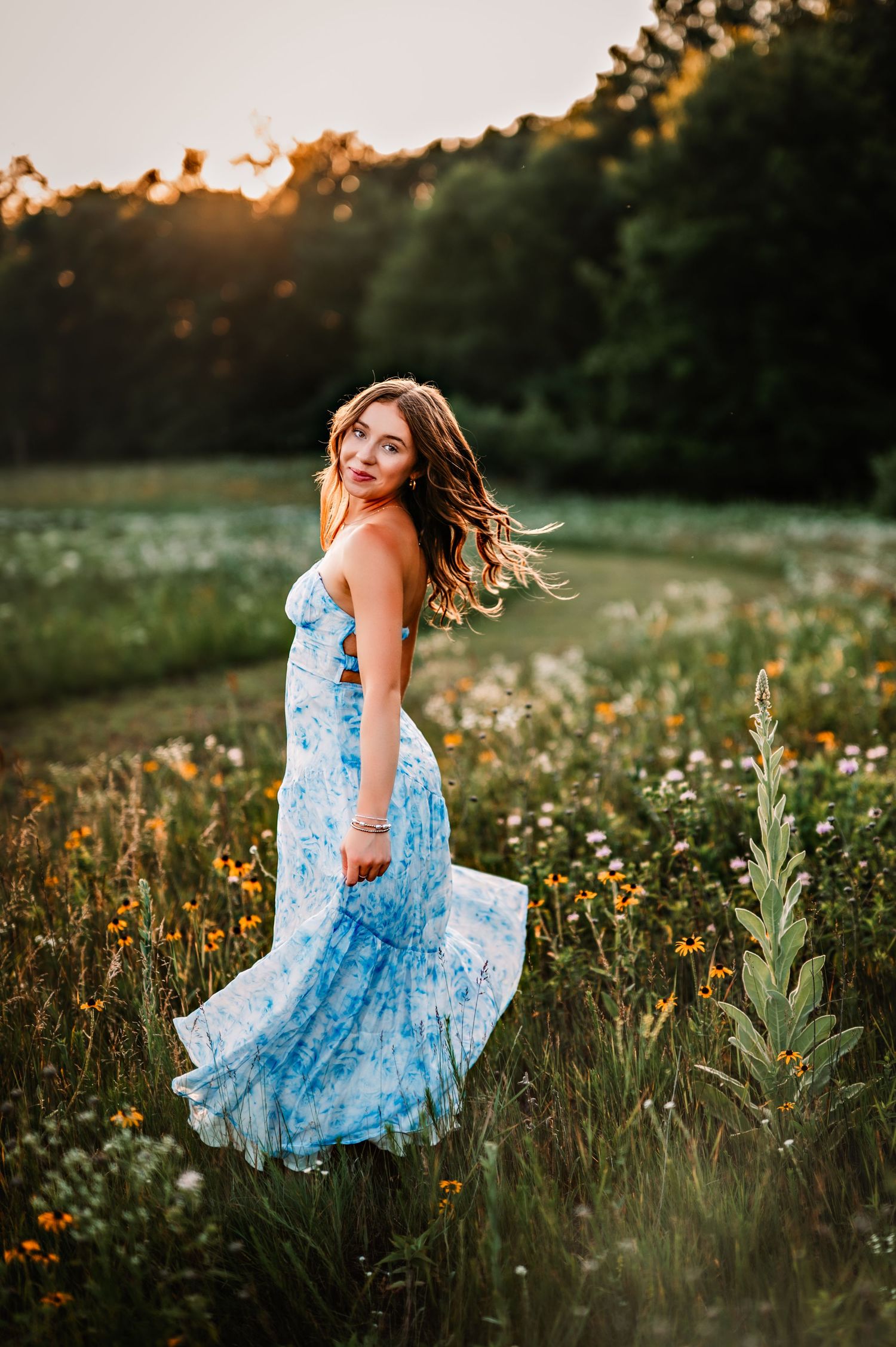 A woman in a flowing blue floral dress twirls in a wildflower meadow at golden hour sunset in Fond du lac, WI