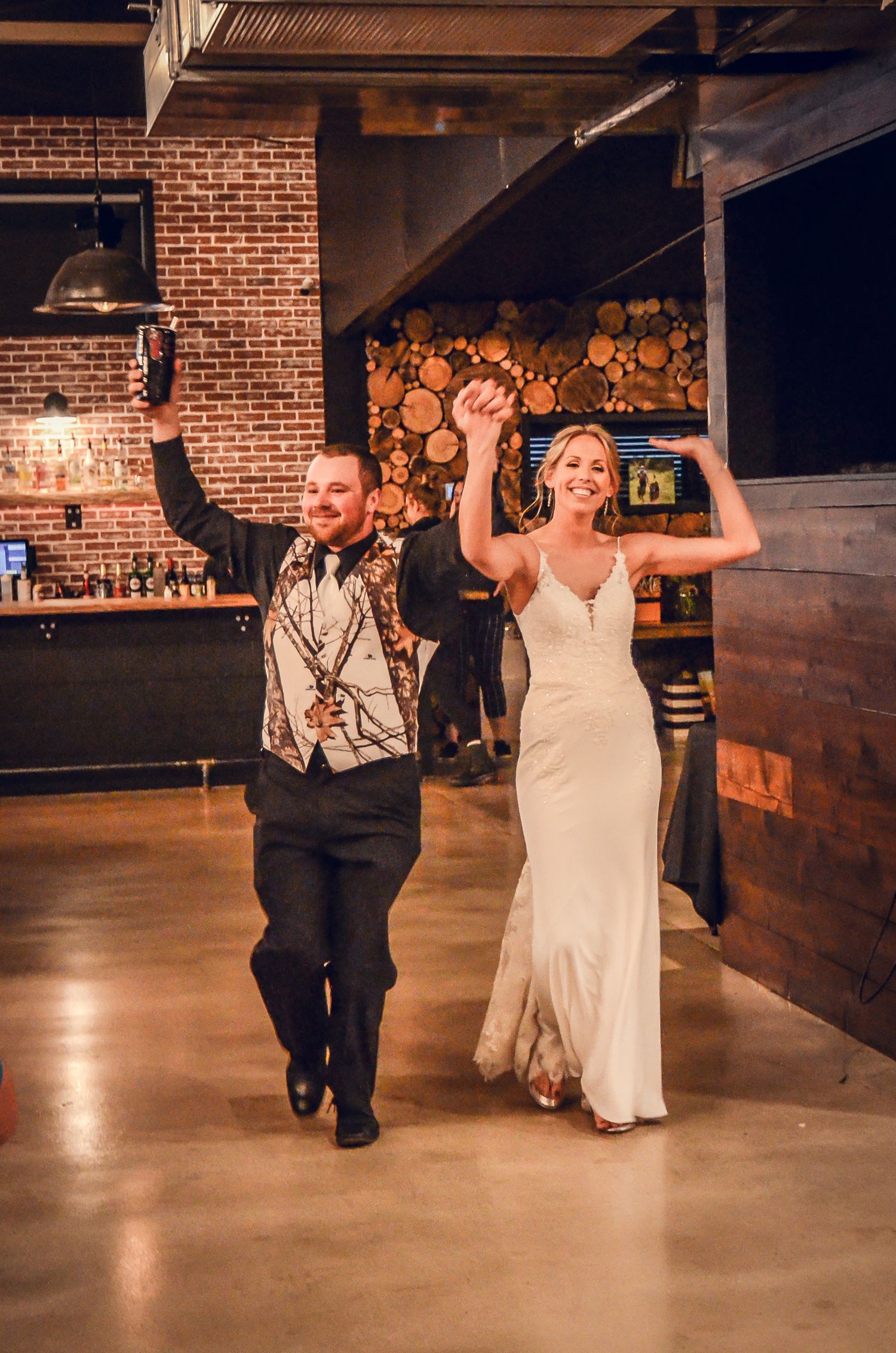 A couple makes their grand entrance at a rustic venue with exposed brick walls and wooden decor.