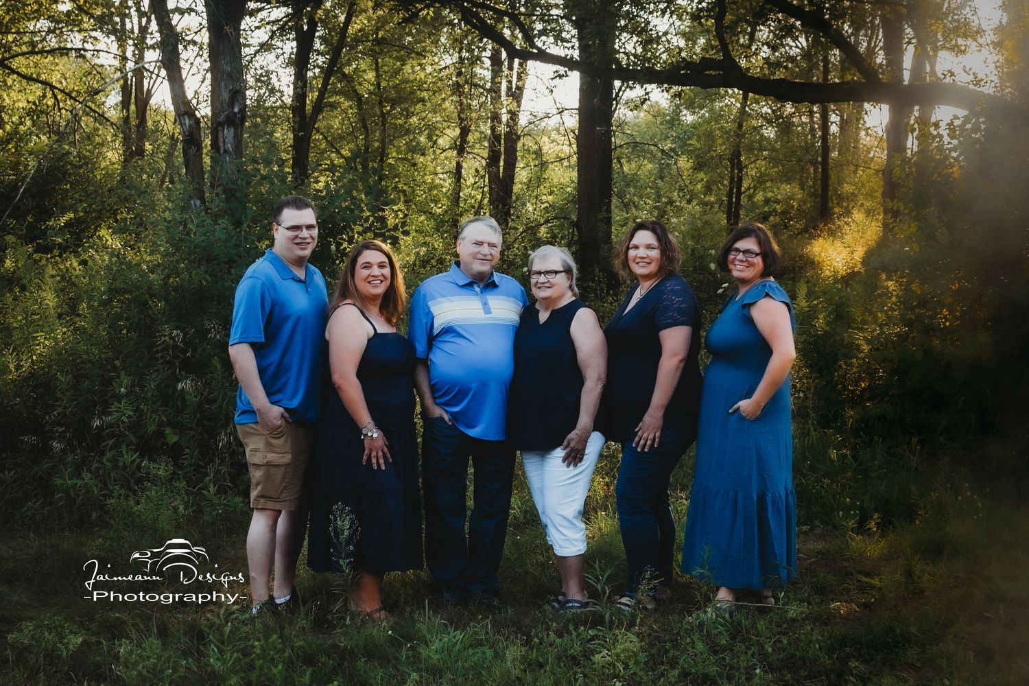 Small family group in coordinating formal attire posed together at sunset in a wooded area.