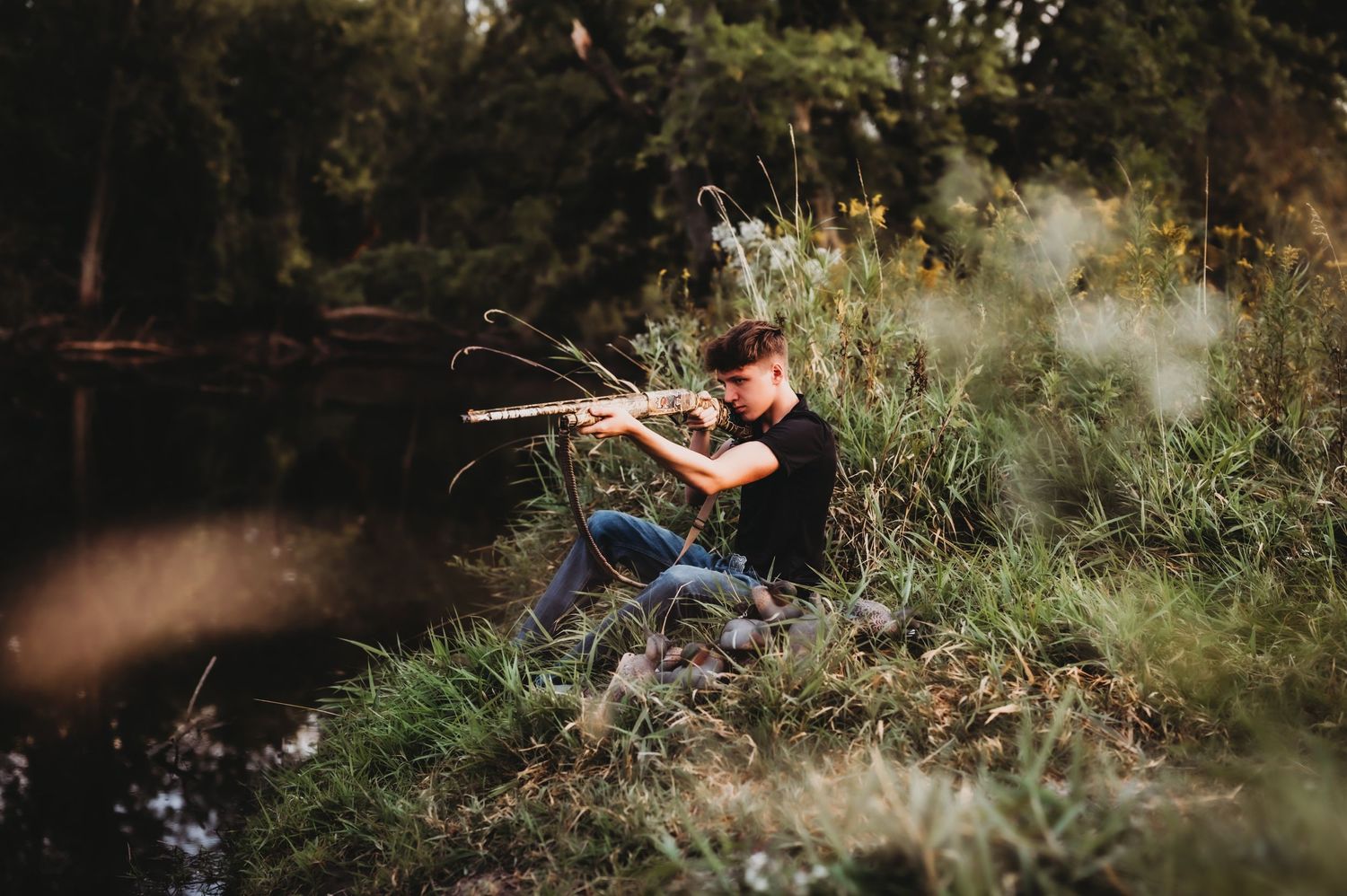 Action shot of person aiming rifle by water's edge in natural setting.