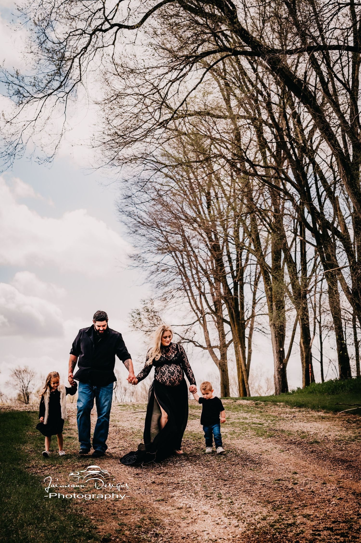 Family walking together on tree-lined path during outdoor photoshoot.