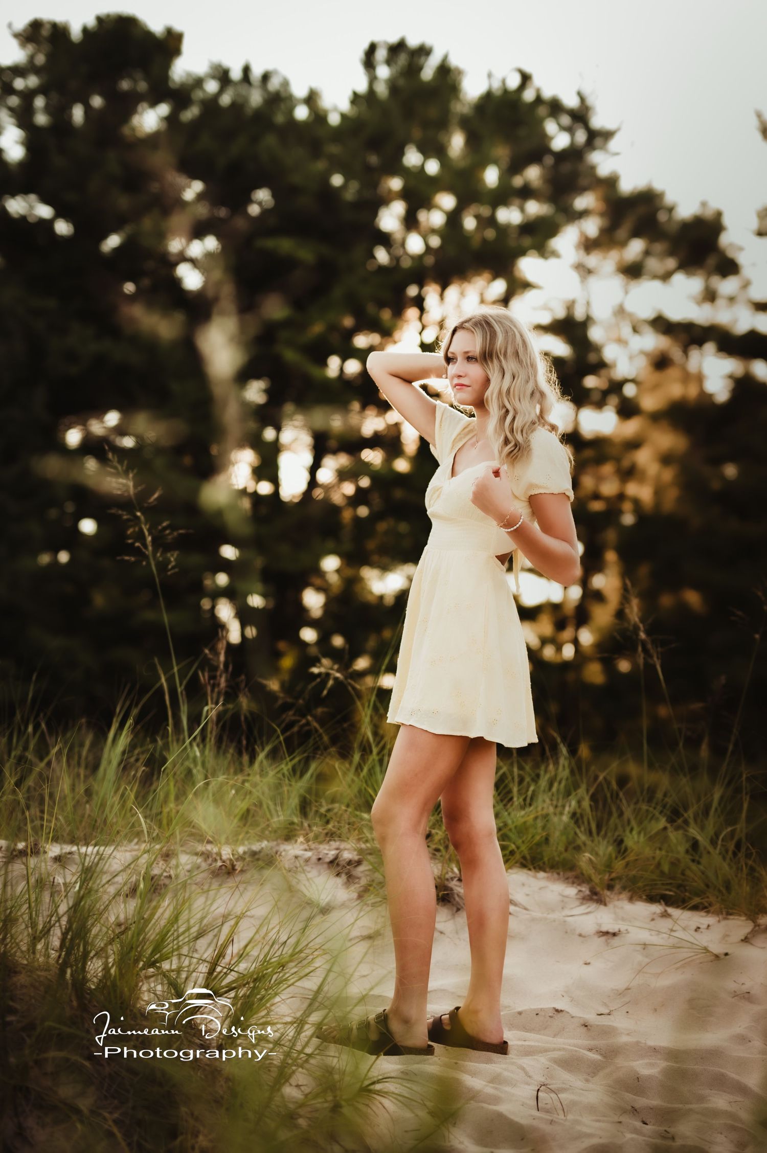 Sunset beach portrait with person in white dress against dark trees.