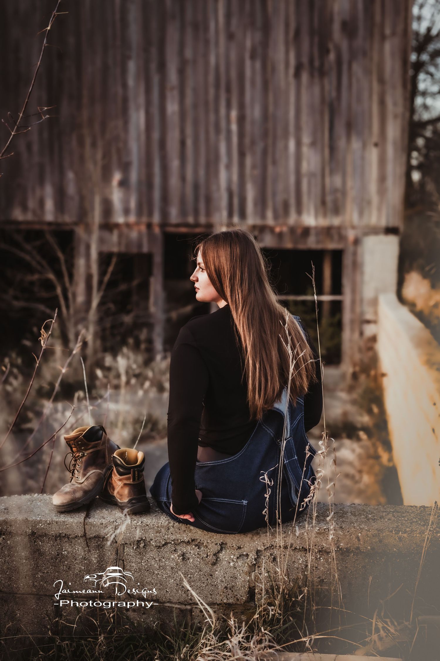 Side profile portrait on concrete ledge with vintage boots beside old barn.
