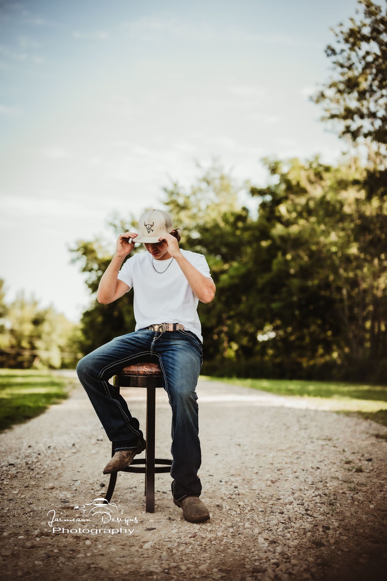 Person in casual attire sitting on a wooden stool outdoors on a gravel path.