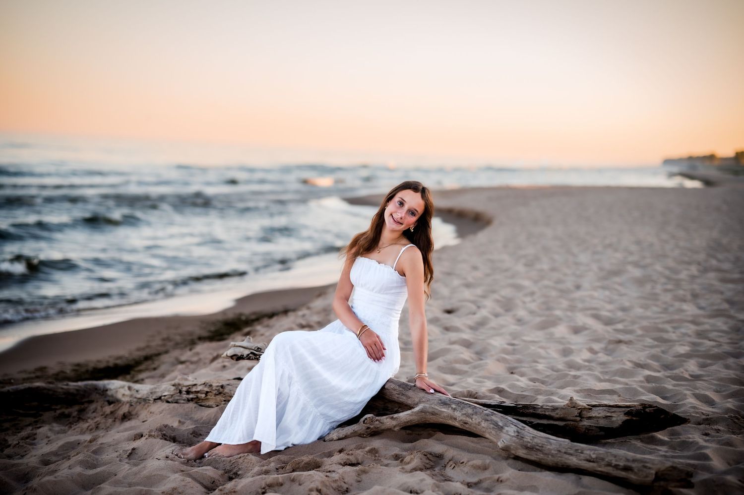 A romantic beach photoshoot series at sunset with flowing white dress and ocean waves in the background in Sheboygan, WI
