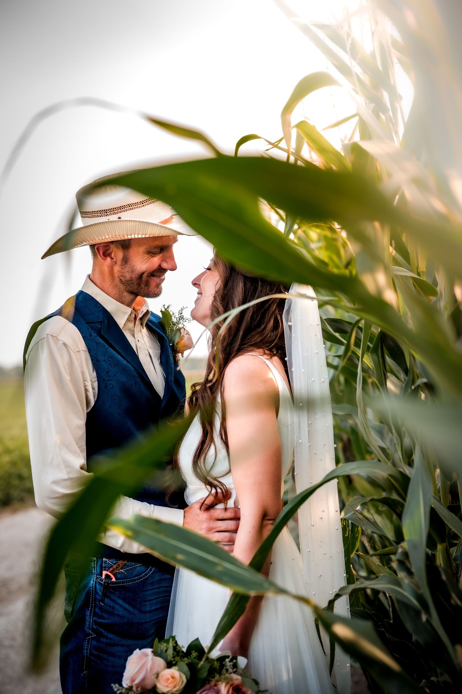 A couple shares an intimate moment among tall green corn stalks during their rustic farm wedding photoshoot.