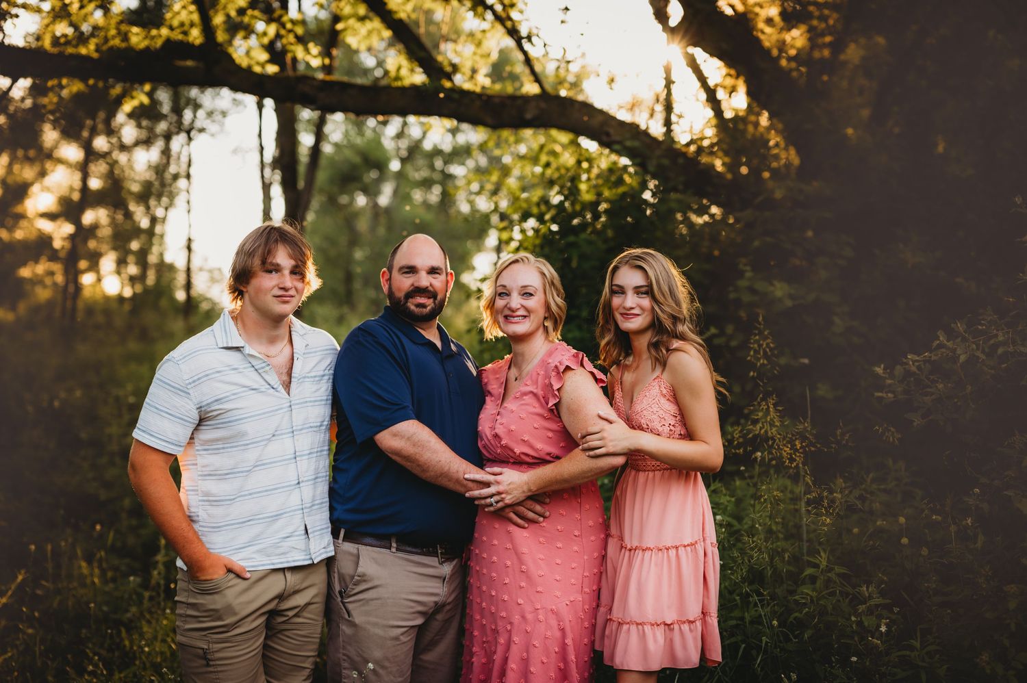 A group poses together outdoors against a backdrop of trees during sunset.