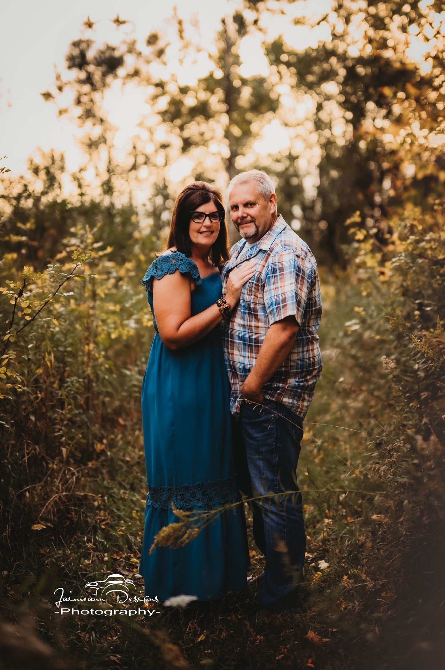 Couple posing together in natural meadow setting with sunset bokeh background.