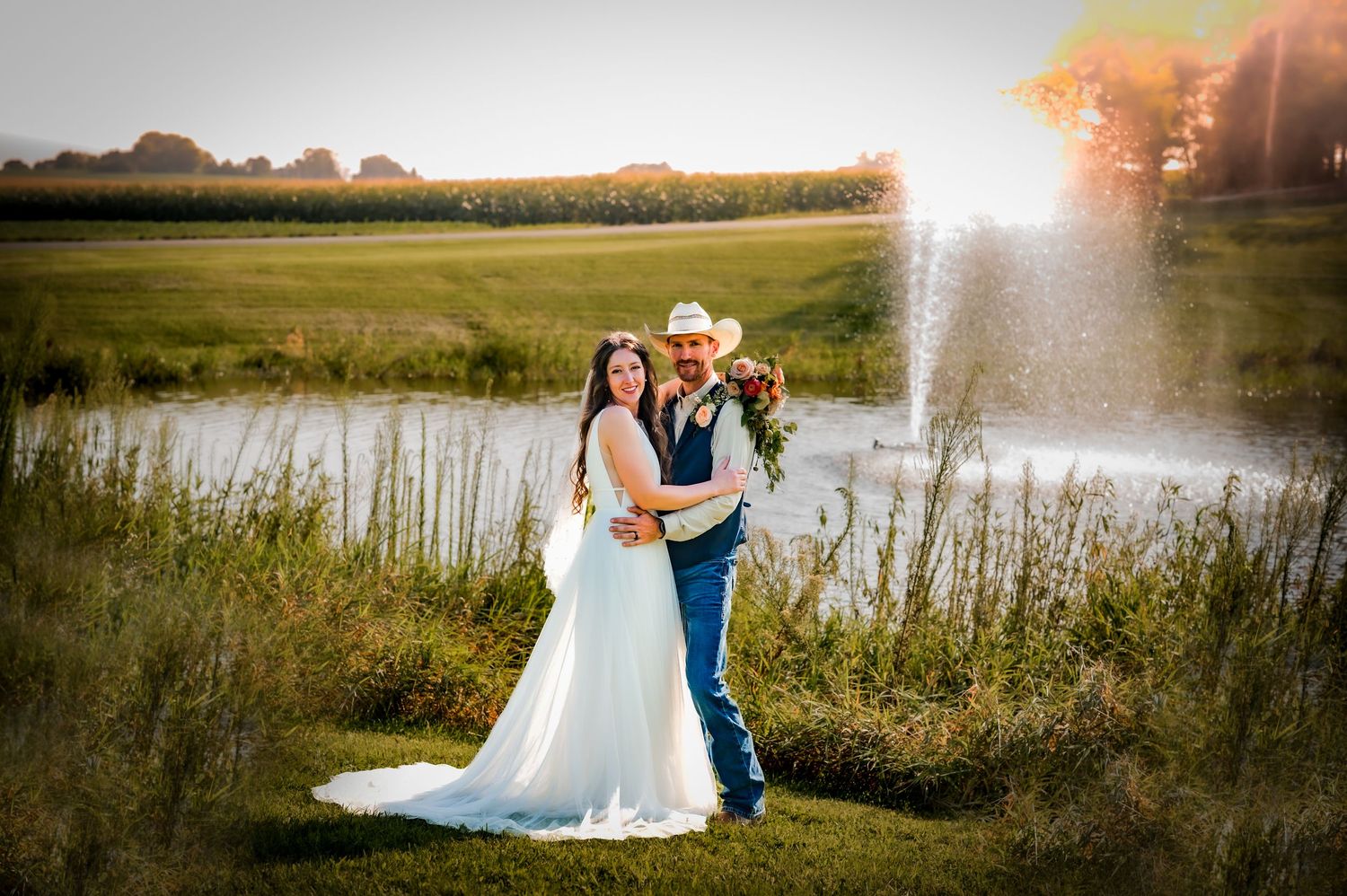 Couple in formal wedding attire embracing in front of scenic pond at sunset with golden light and tall grasses. Oconomowoc, WI Wedding Barn