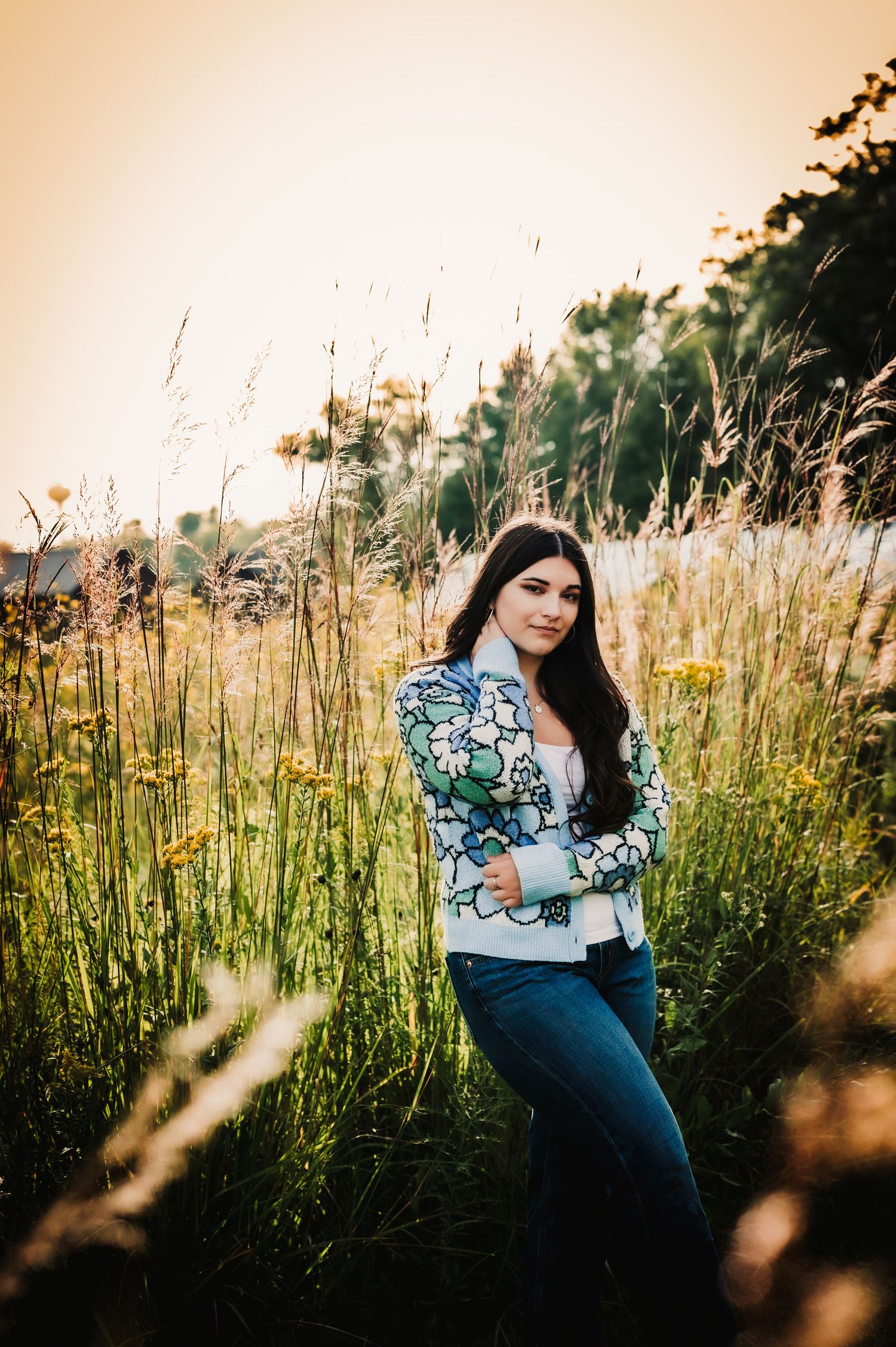 Floral print top and jeans outfit amid tall grasses at golden hour.