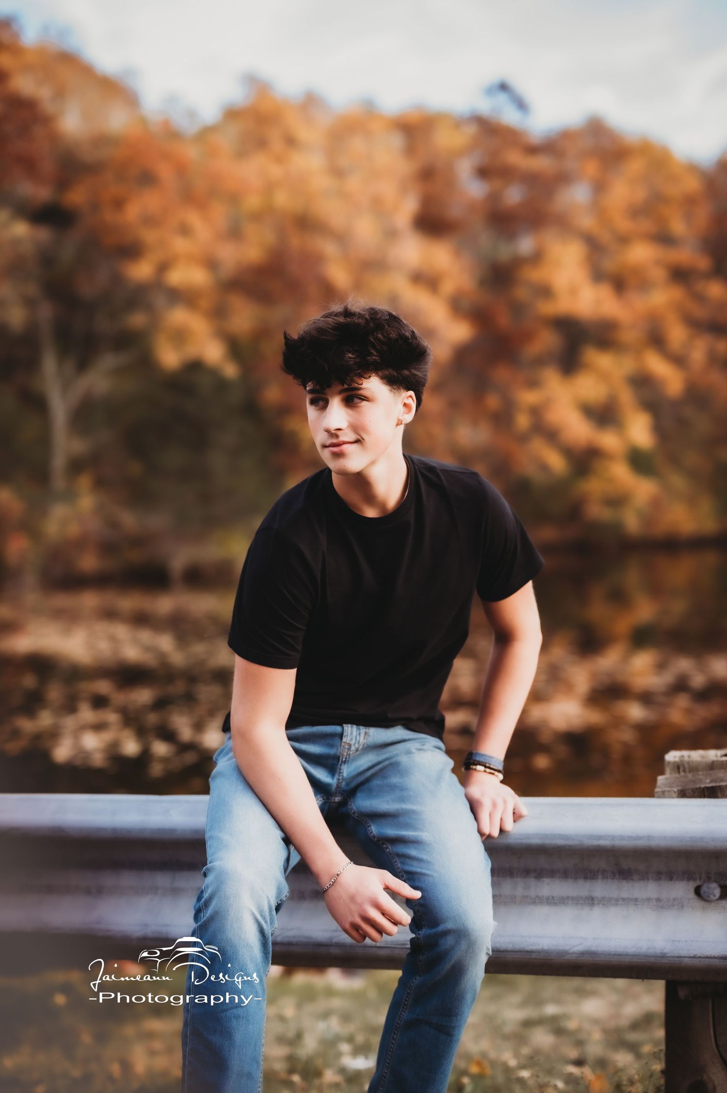 Portrait photograph against autumn foliage background featuring casual black t-shirt and jeans on park bench.