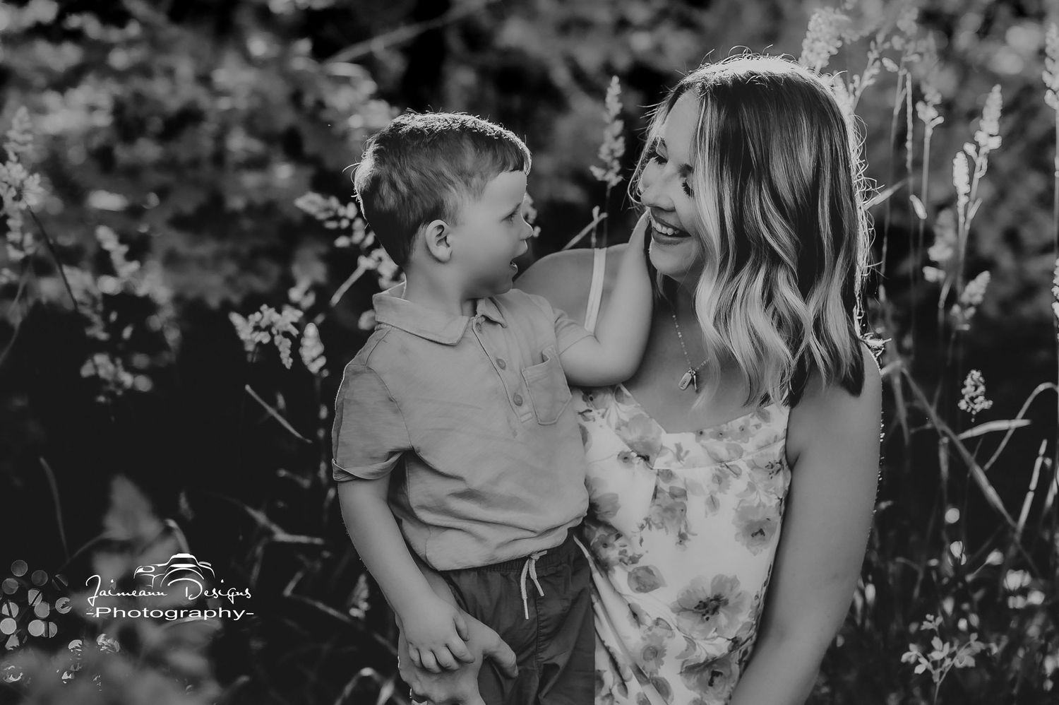 Black and white candid portrait of mother and child sharing laughter in natural setting.