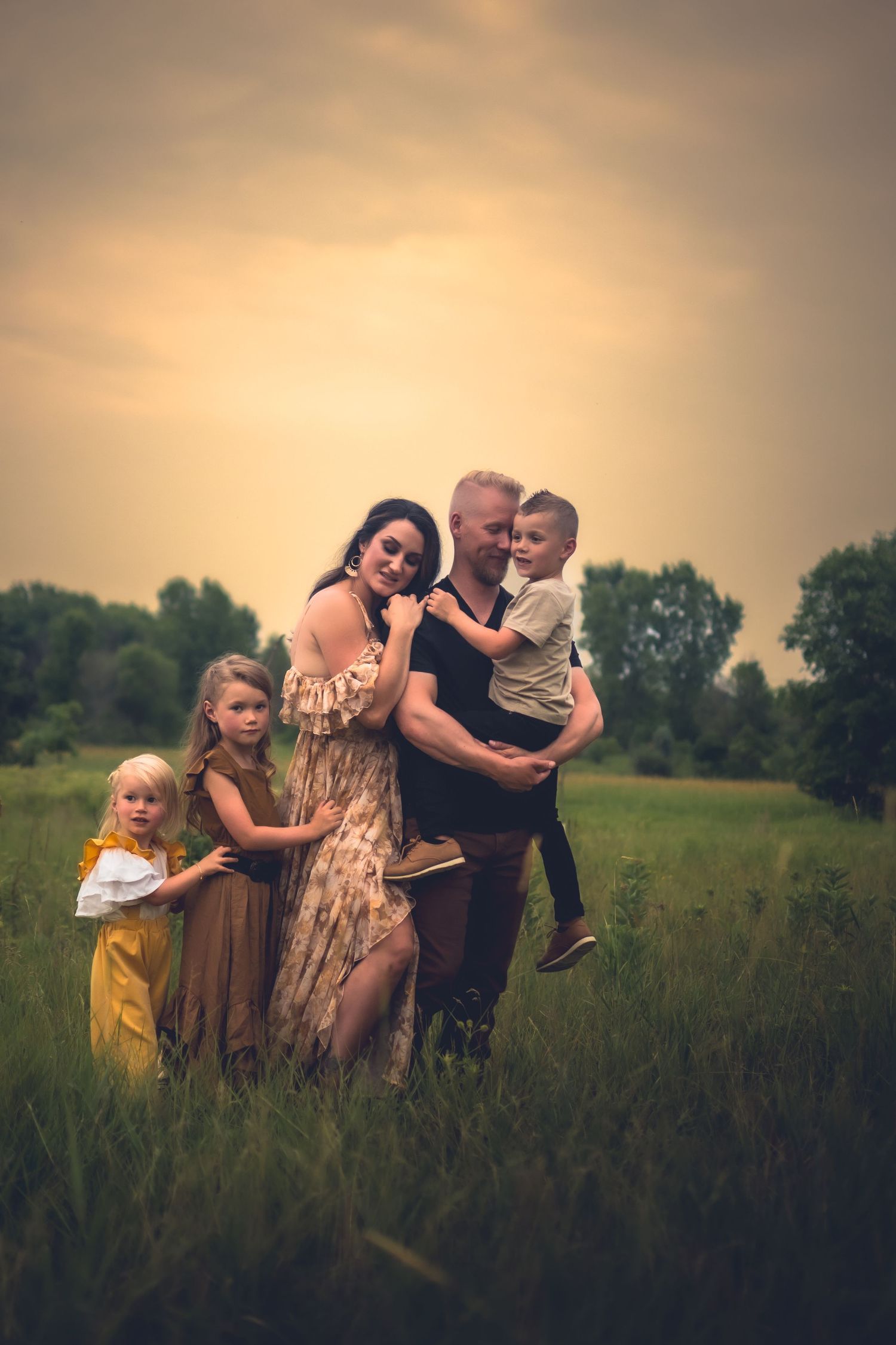 Family stands together in tall grass field during sunset golden hour.