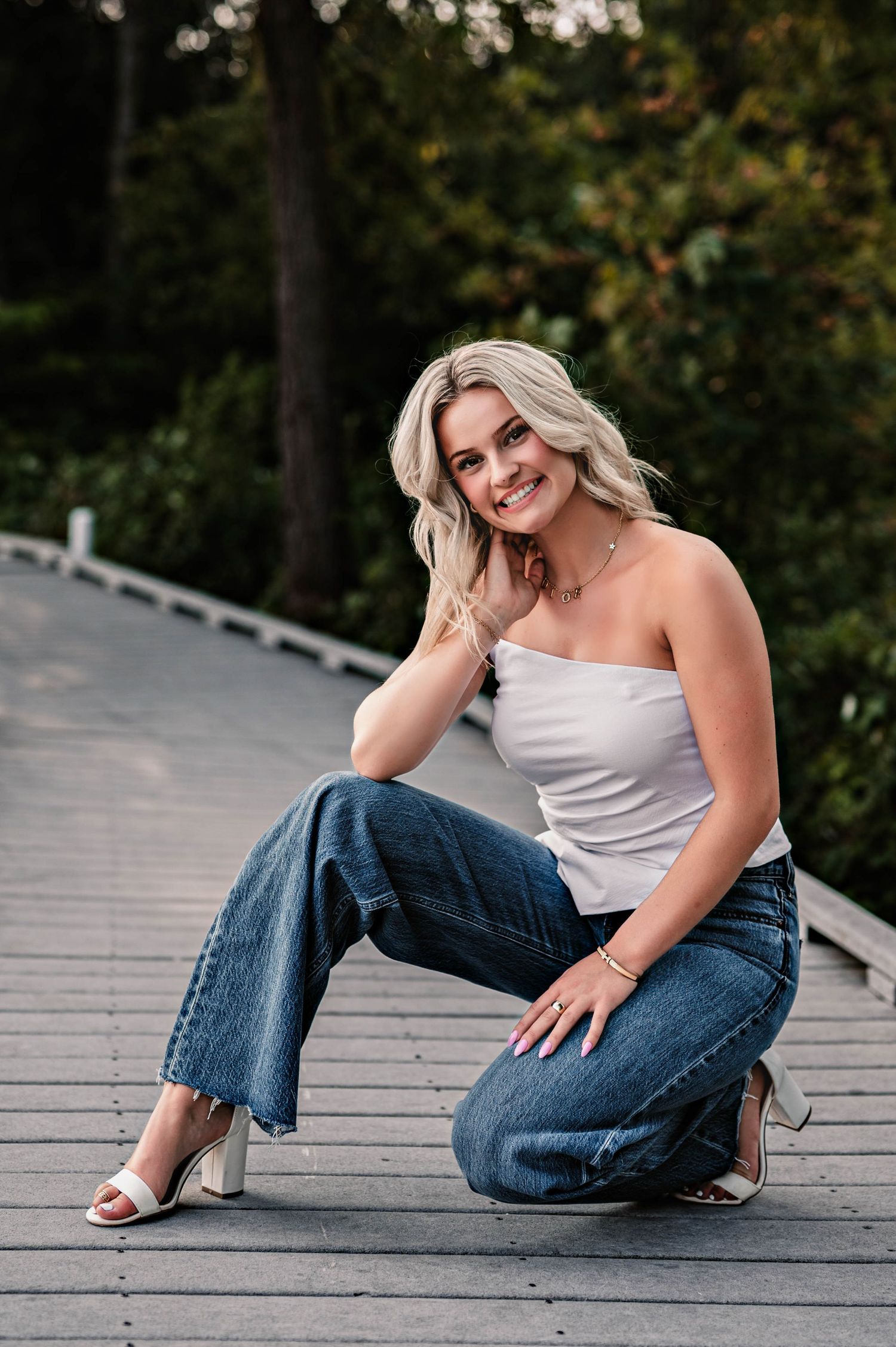 A person in a white top and blue jeans poses playfully on a wooden deck in an outdoor setting, Near Menomonee Falls, WI
