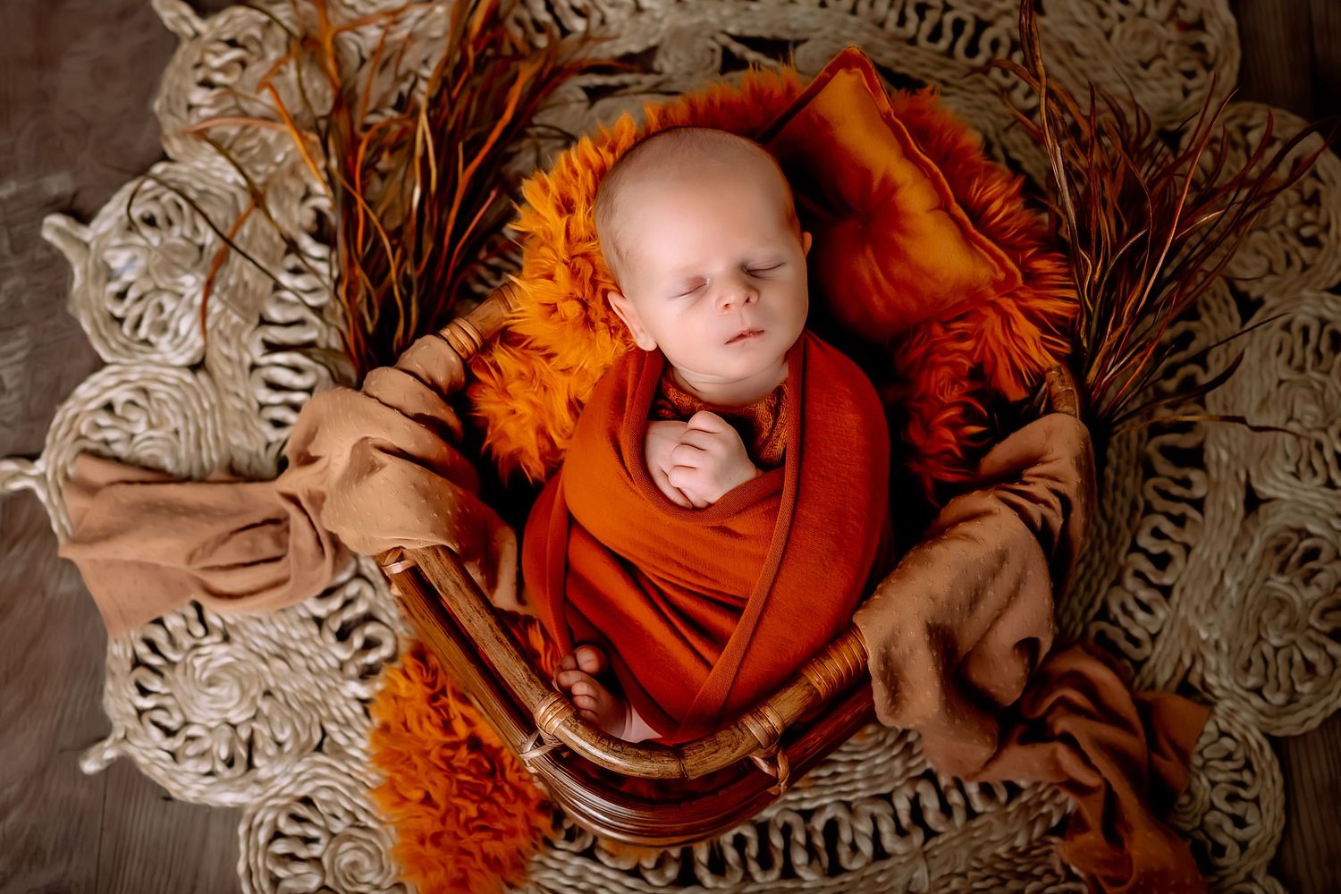 A sleeping baby wrapped in orange fabric lies on a textured gray blanket with floral patterns signature newborn session in Kewaskum, WI stud