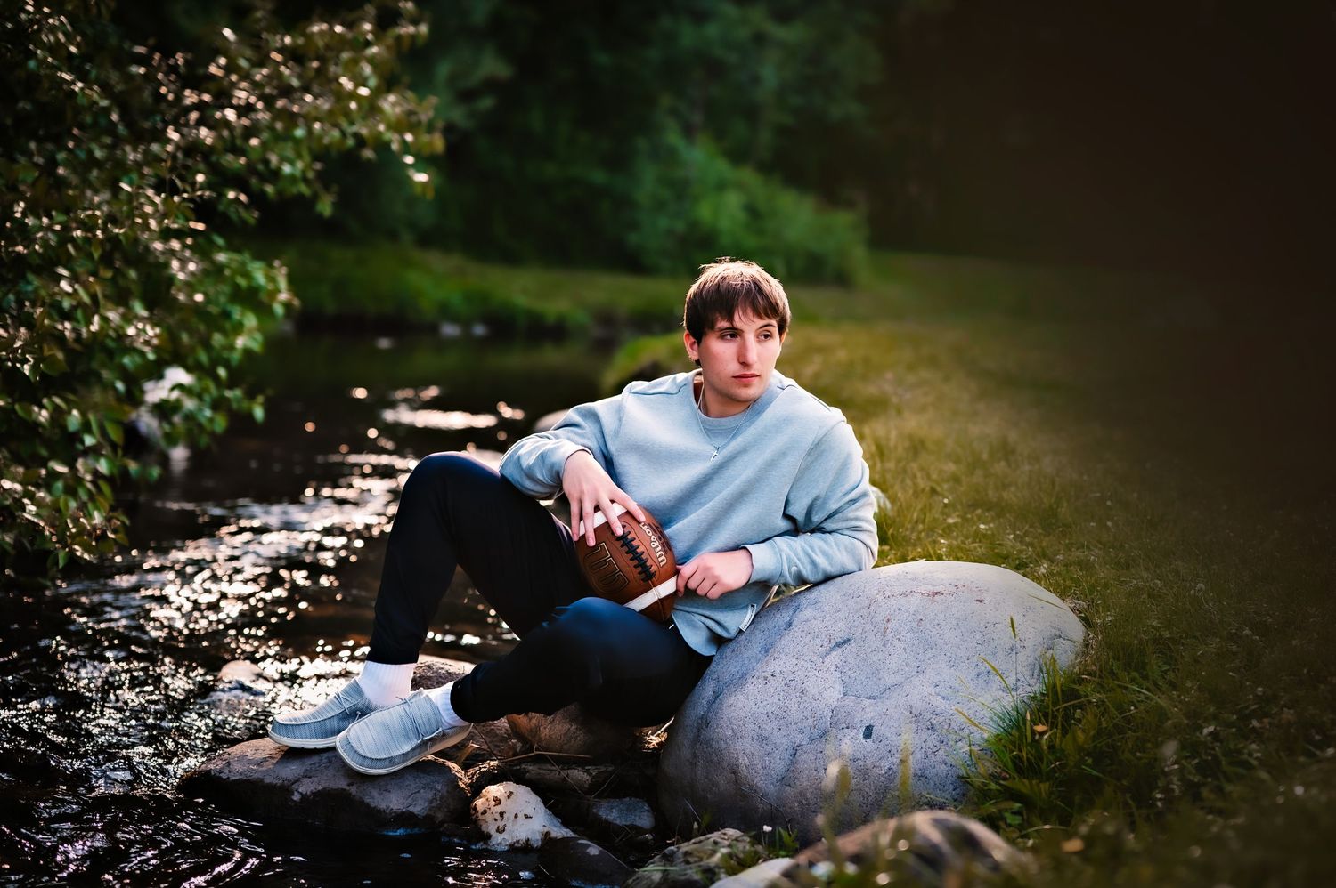 Someone sits on a large boulder by a stream reading a book while wearing a light blue sweater in a peaceful outdoor setting, Regnar Park, WI