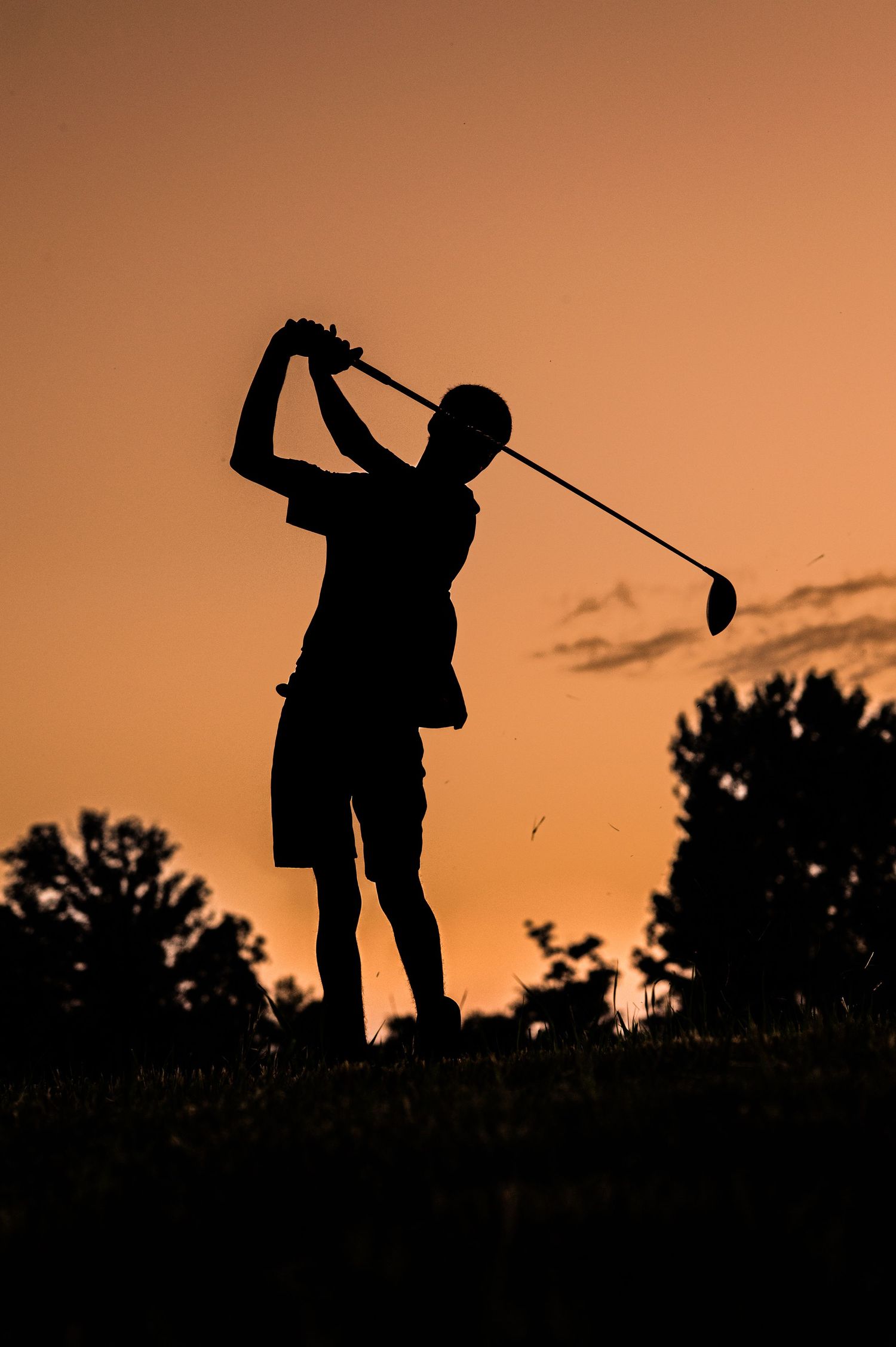 Silhouettes of golfers swinging clubs against an orange sunset sky.