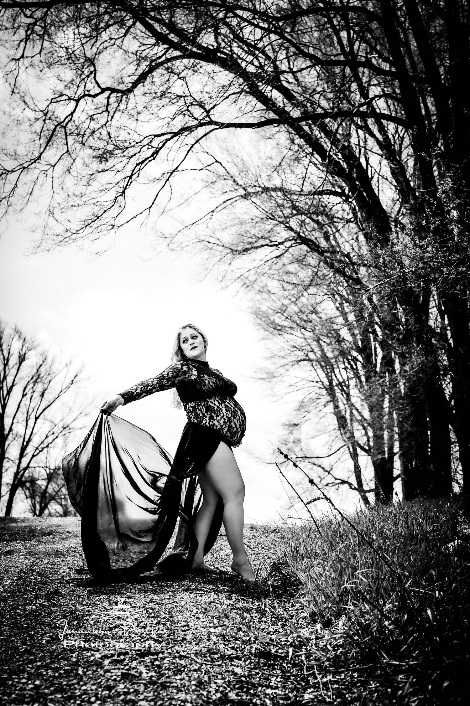 Black and white maternity portrait on forest path with dramatic dress movement.