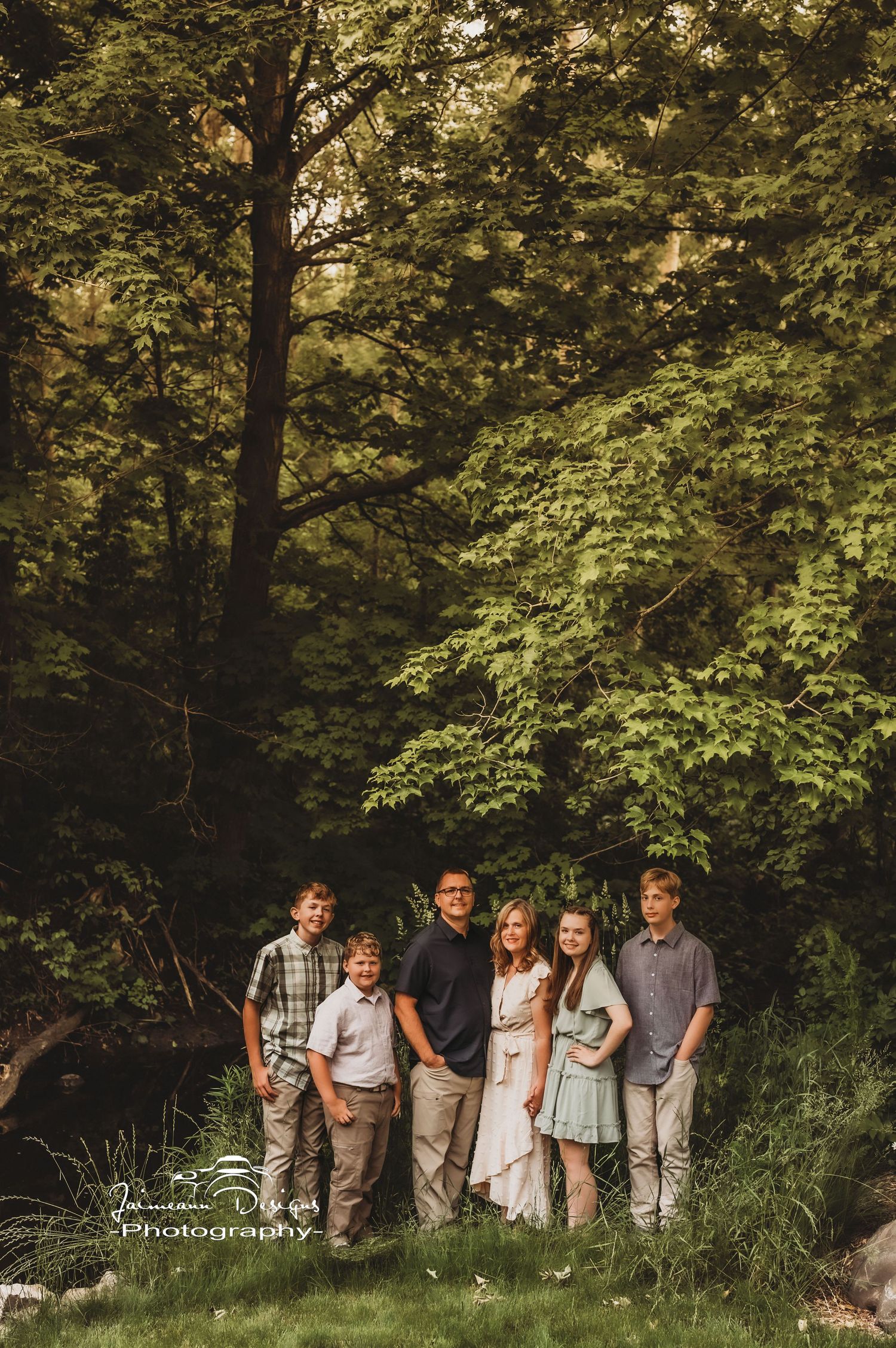 A family group portrait in a lush green forest setting with natural lighting.