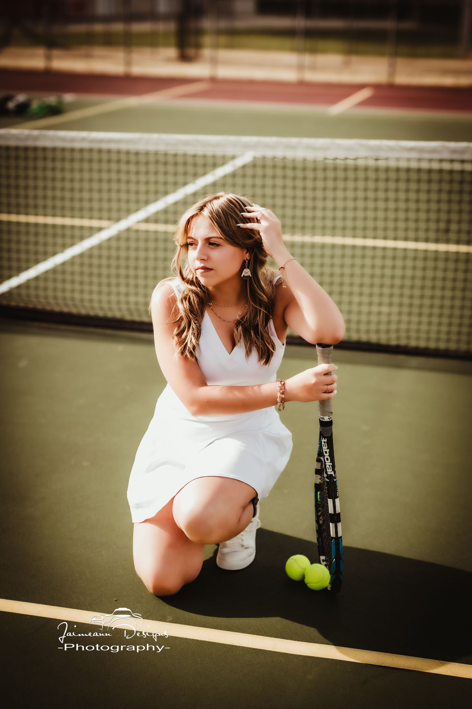 Person posing on tennis court in white dress with racket and tennis balls.