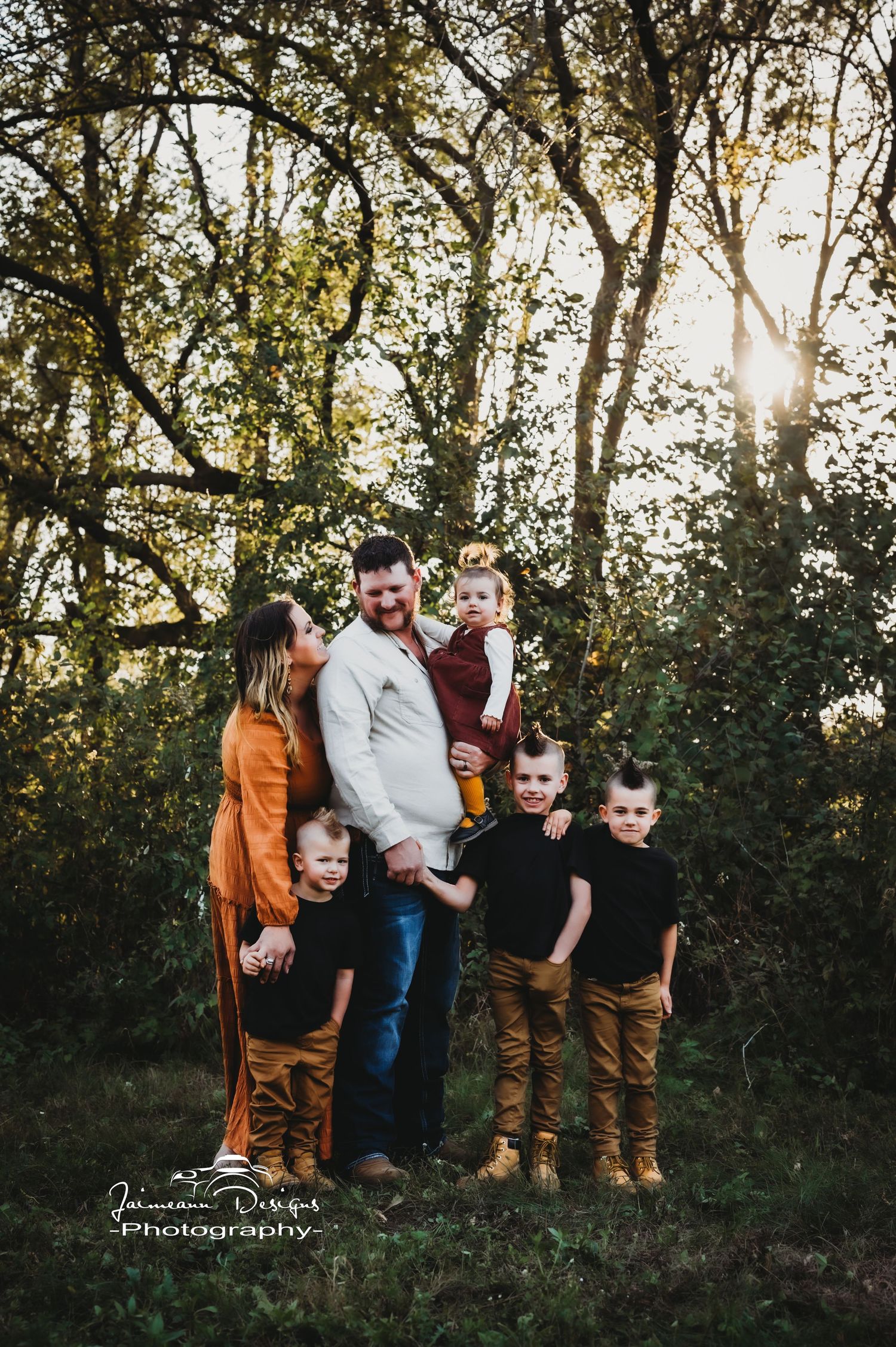 A family portrait taken at golden hour in a forest setting with sunlight peeking through the trees.