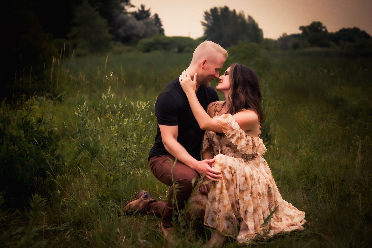Couple sharing intimate moment in grassy field during golden hour.