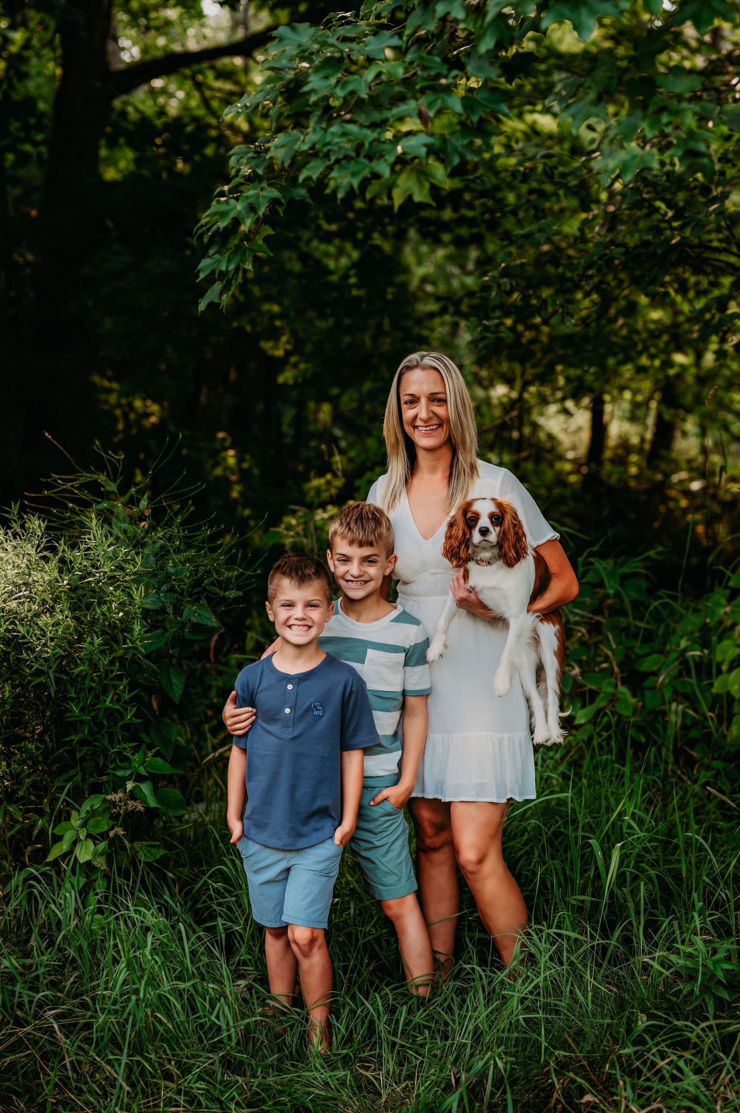 Family and their Cavalier King Charles Spaniel puppy enjoying a summer photoshoot in a lush green outdoor setting near Milwaukee, WI