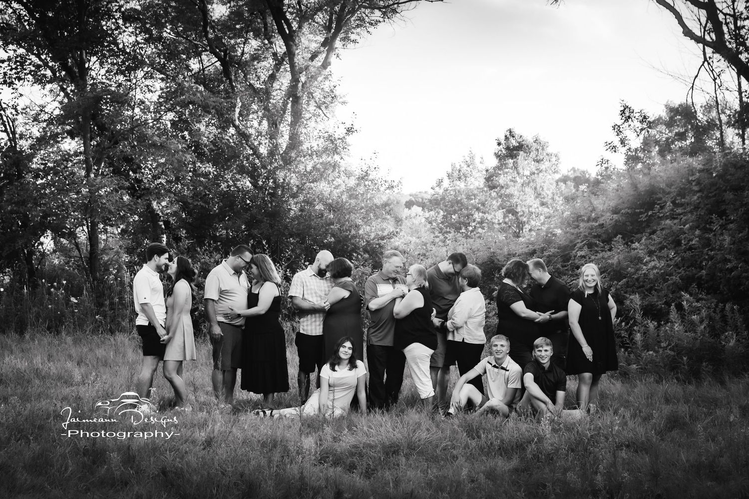 Black and white photo of a large group posed casually in a meadow surrounded by trees.