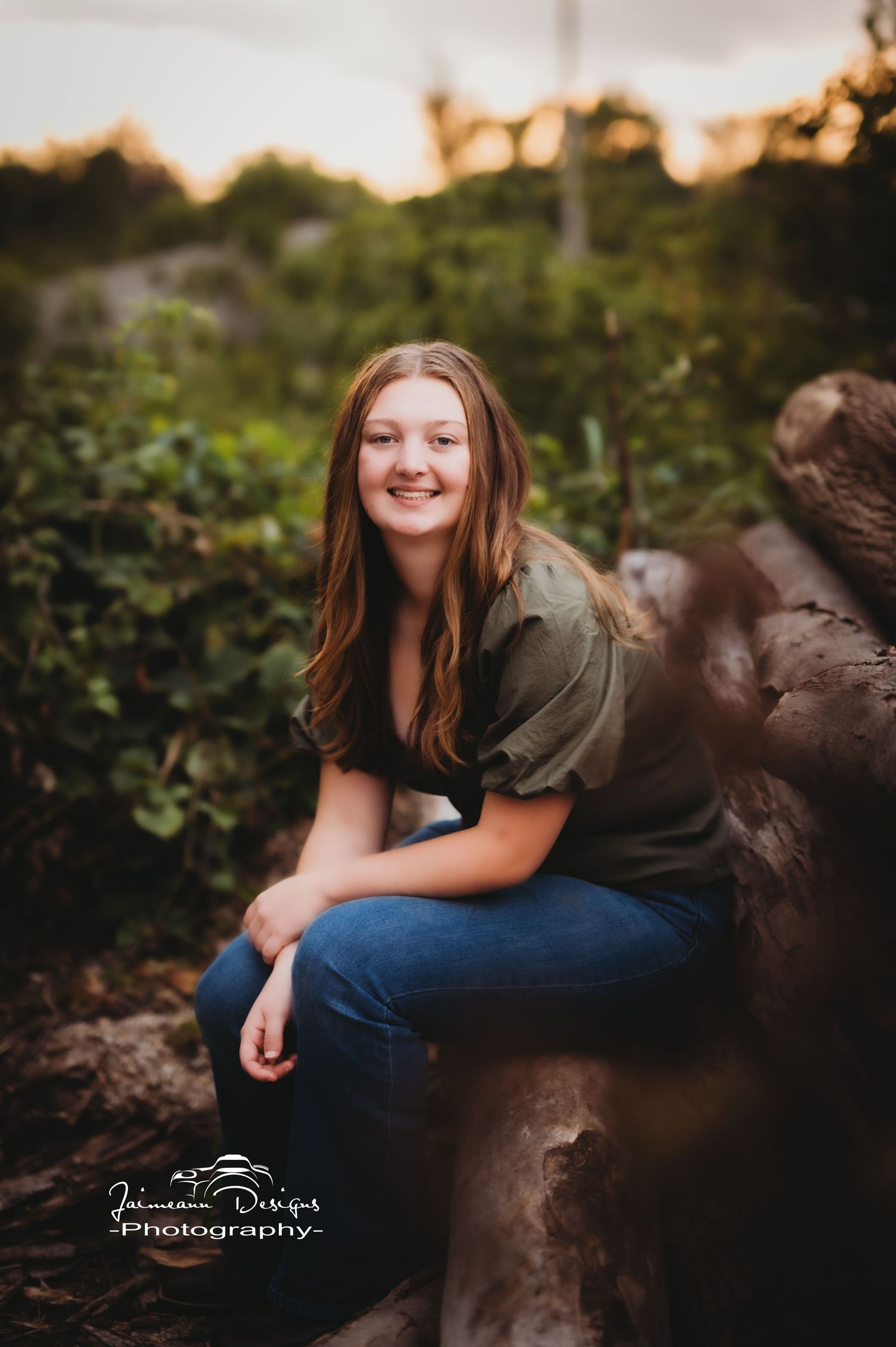 Casual portrait on a wooden log with greenery and sunset lighting in the background.