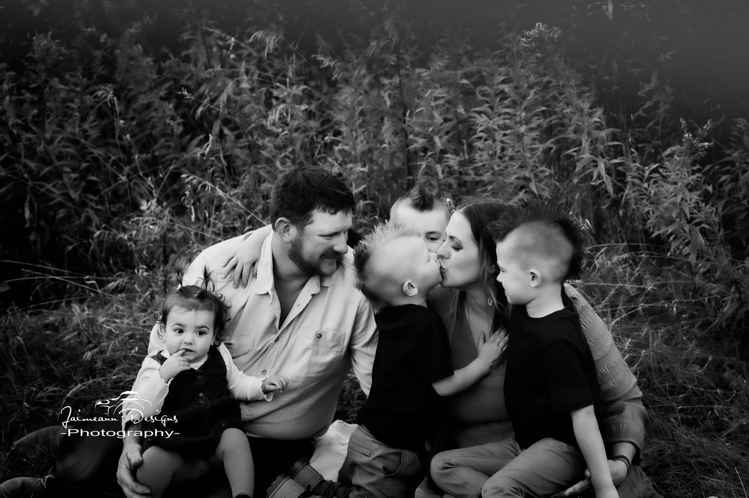 A black and white portrait of a family sitting close together outdoors.