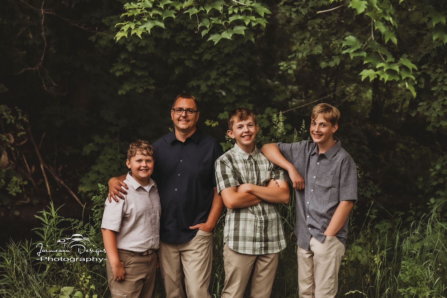 A group portrait of four people standing together in casual attire against a wooded background.