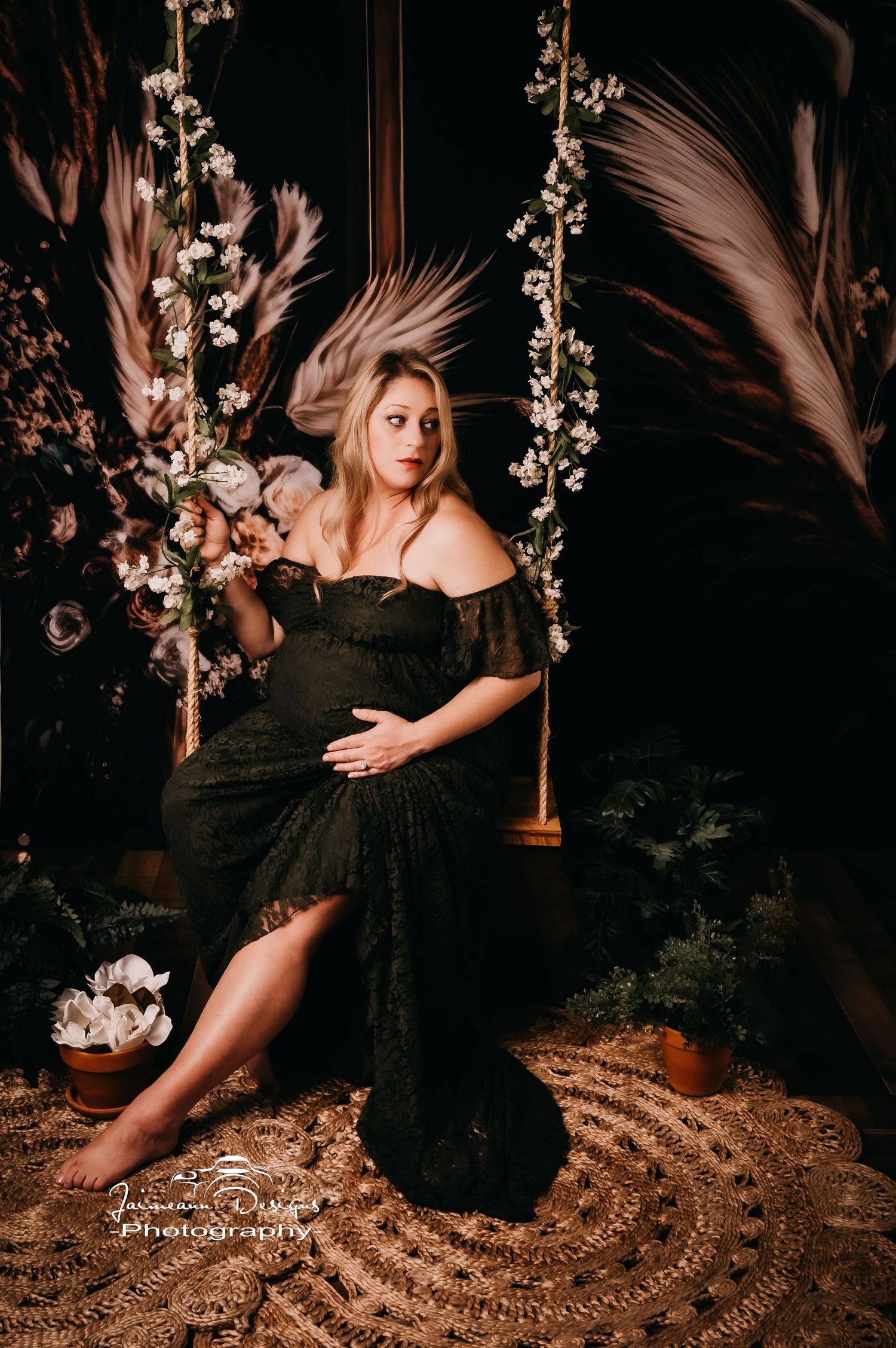 Artistic maternity photo with floral swing and flowing black dress in moody setting.