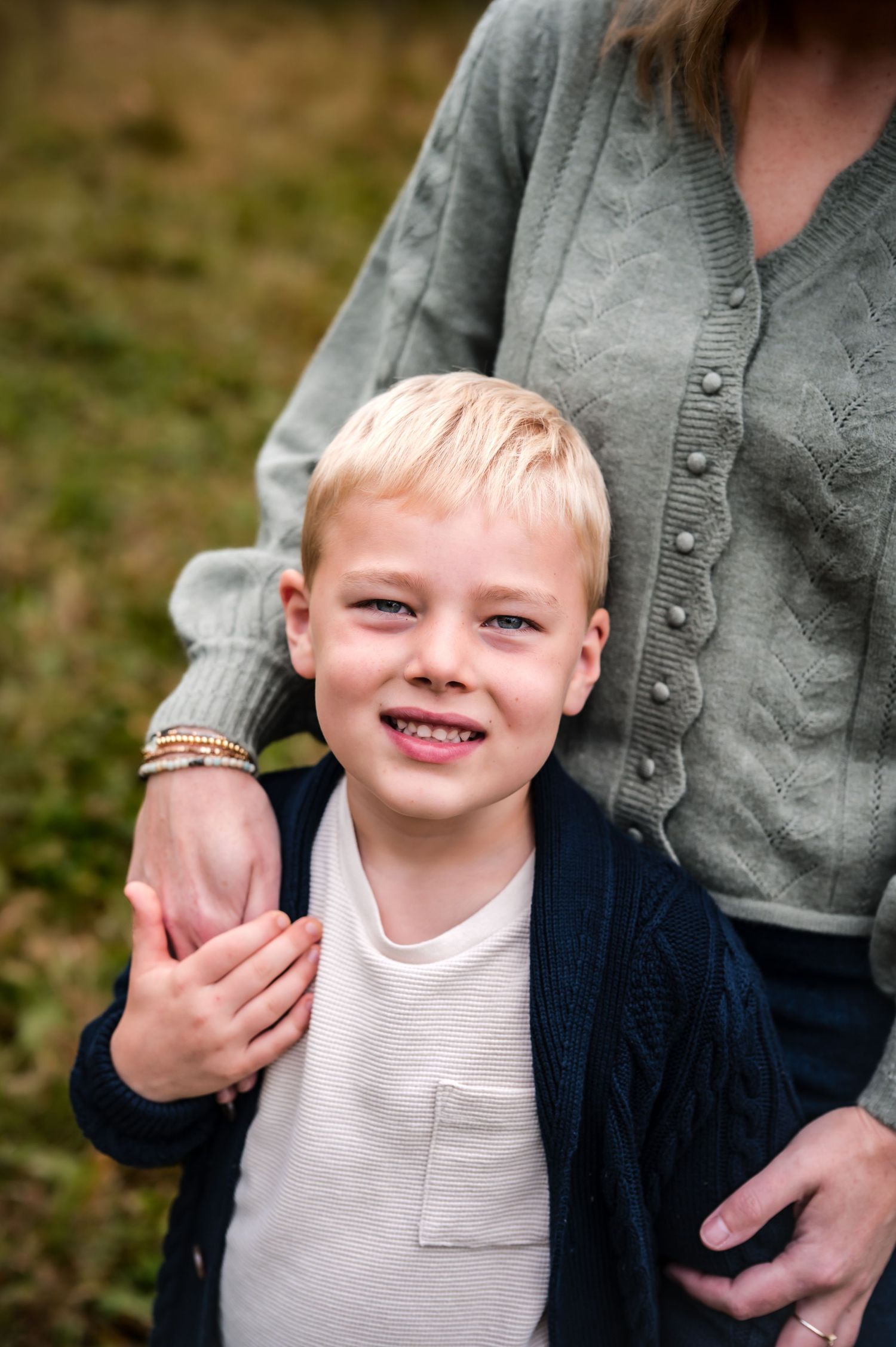A child in a white shirt and navy cardigan smiles warmly while being embraced by someone in a sage green sweater near Mequon, WI