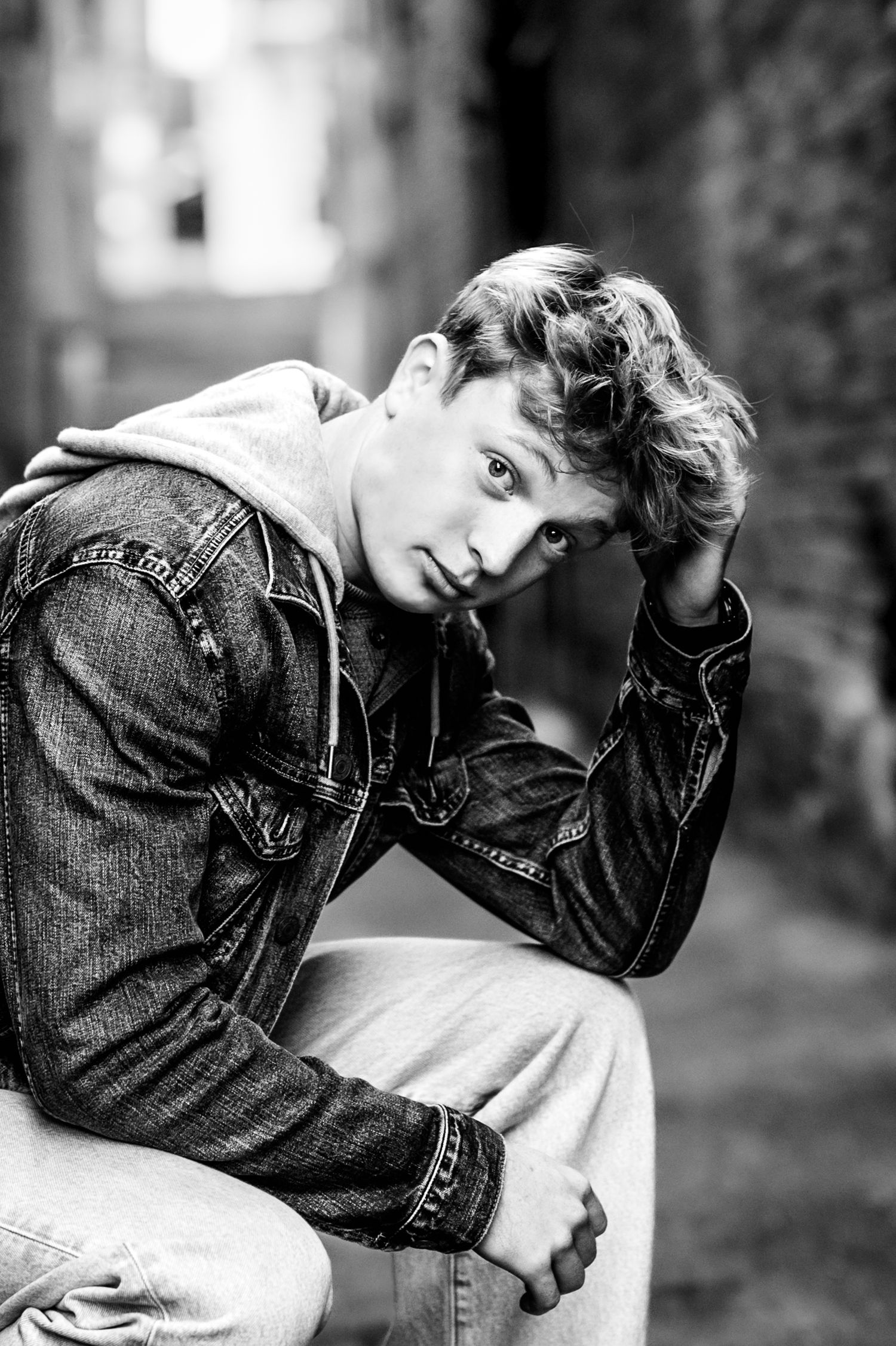 Black and white artistic portrait series showing someone in denim jacket posing against dark background, in West Bend, WI Alley