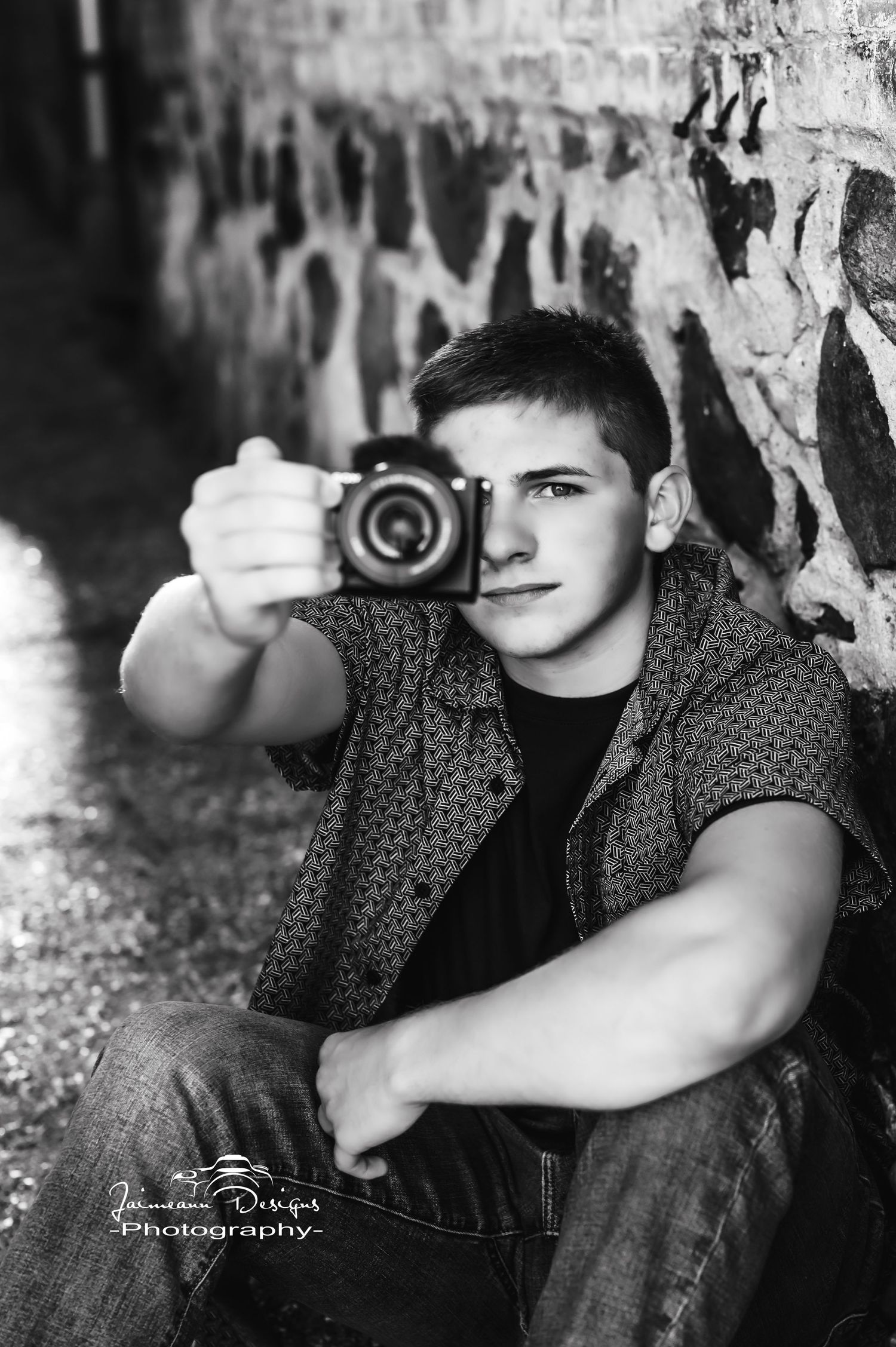 Black and white portrait holding a camera against a graffiti wall.
