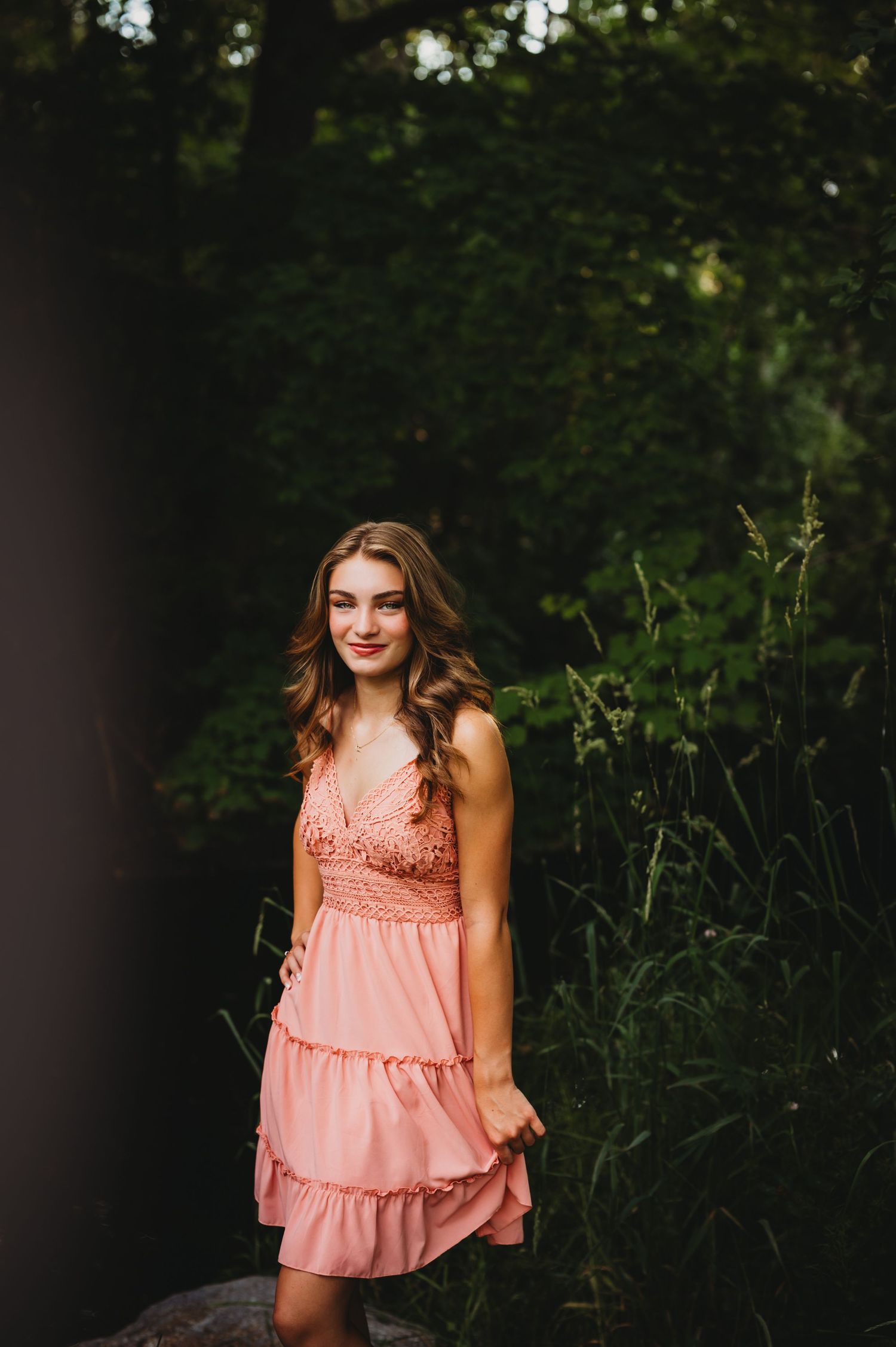 Person in coral summer dress poses outdoors against lush green foliage background.