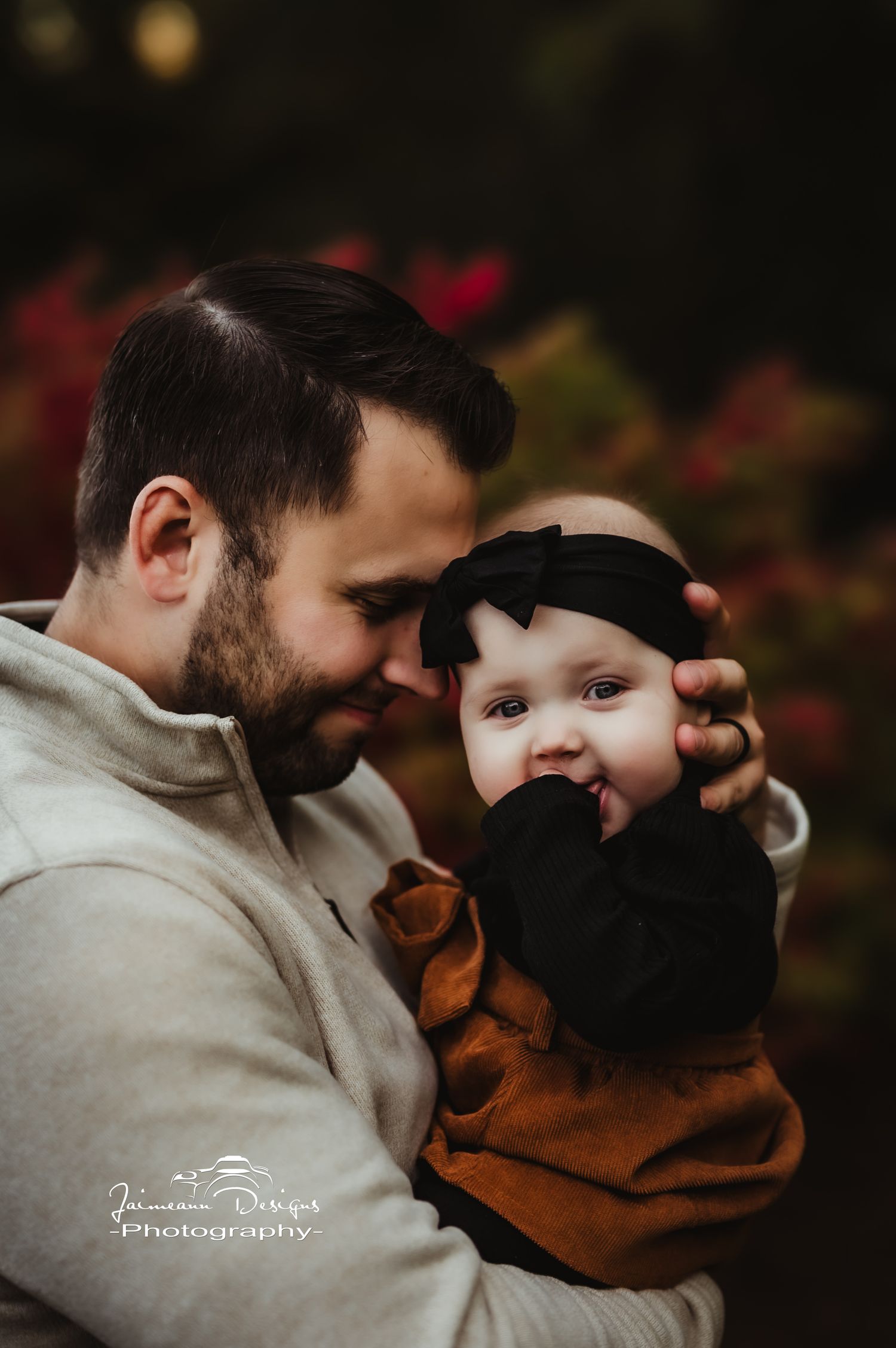 A tender moment between parent and baby in warm autumn clothing against dark background.