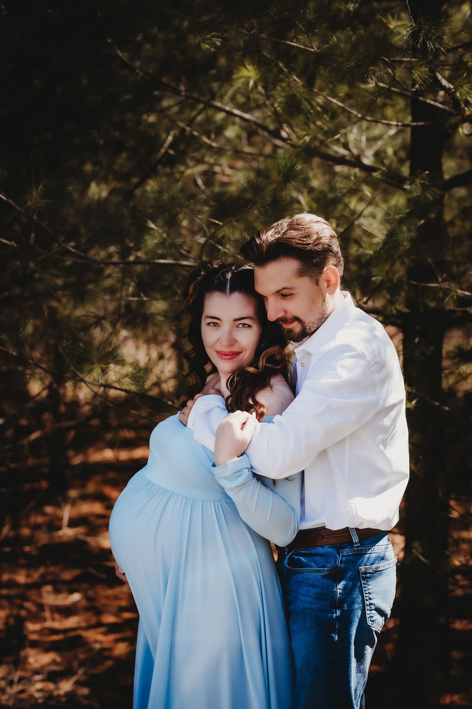 Romantic outdoor maternity photo of a couple embracing under tree branches.