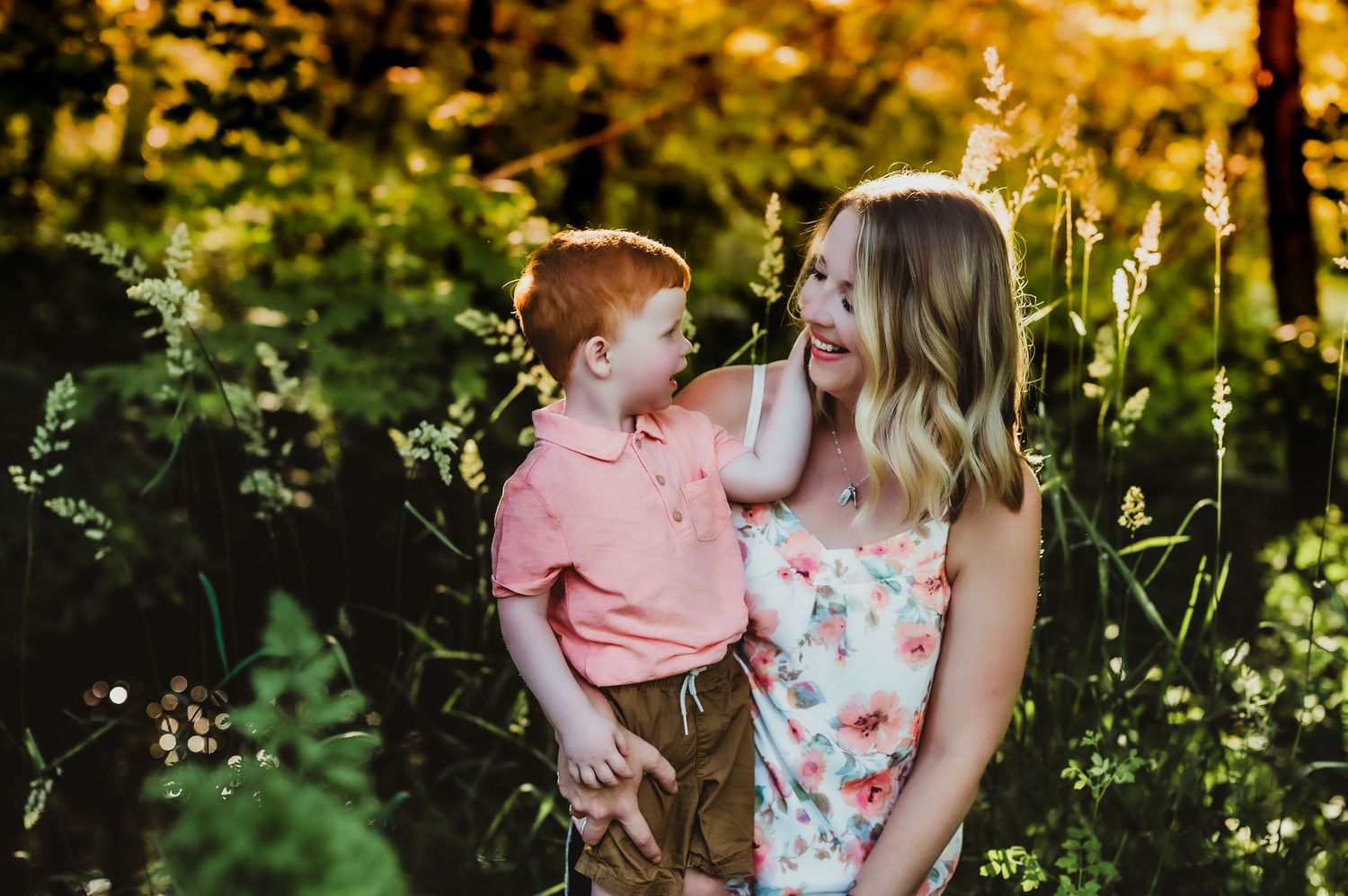 An outdoor portrait showing joyful interaction between parent and child in a sun-dappled forest setting.