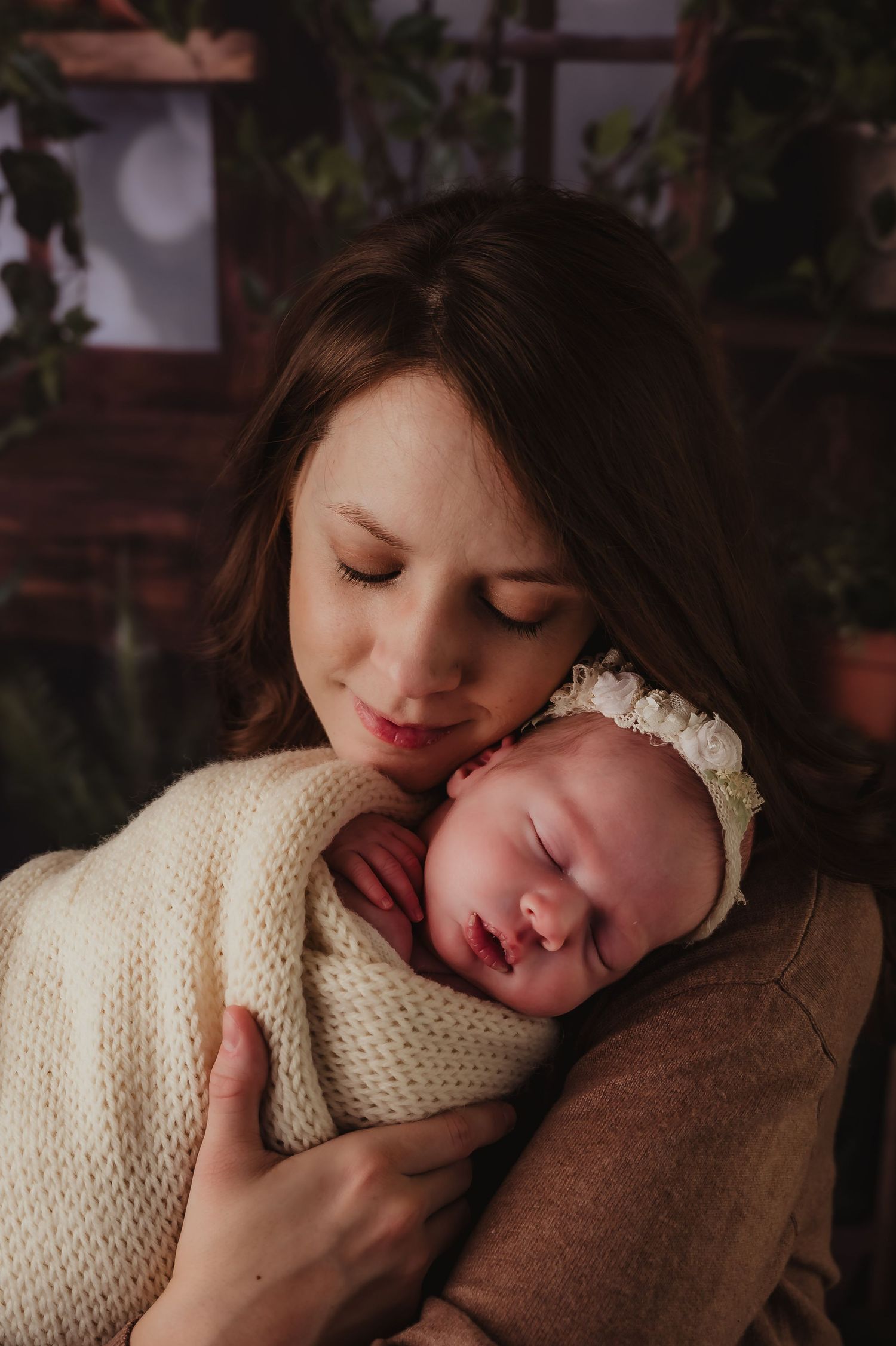 Mother cradling sleeping newborn wrapped in cream knit blanket in intimate indoor portrait.