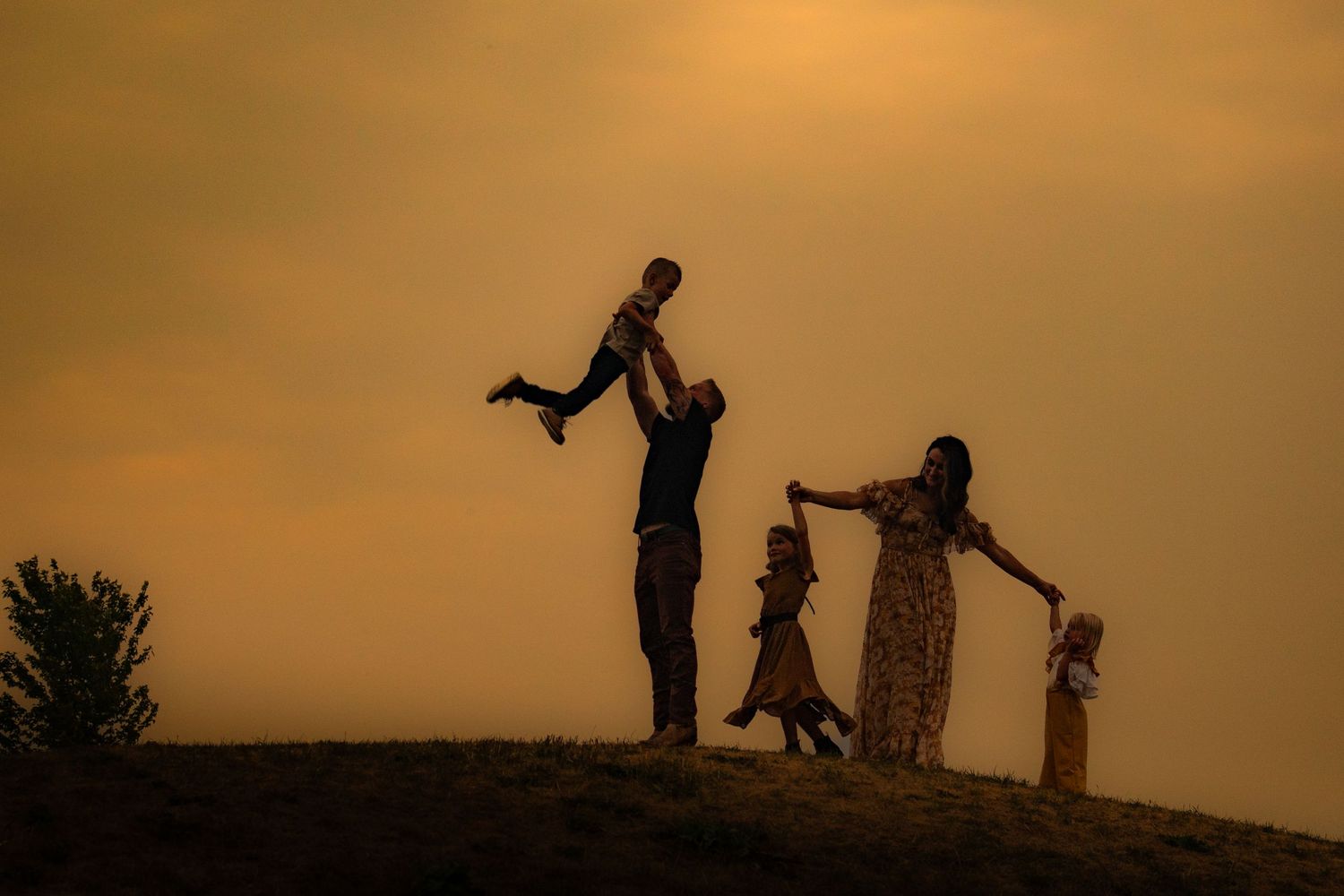Silhouettes of family playing and jumping together against orange sunset sky.