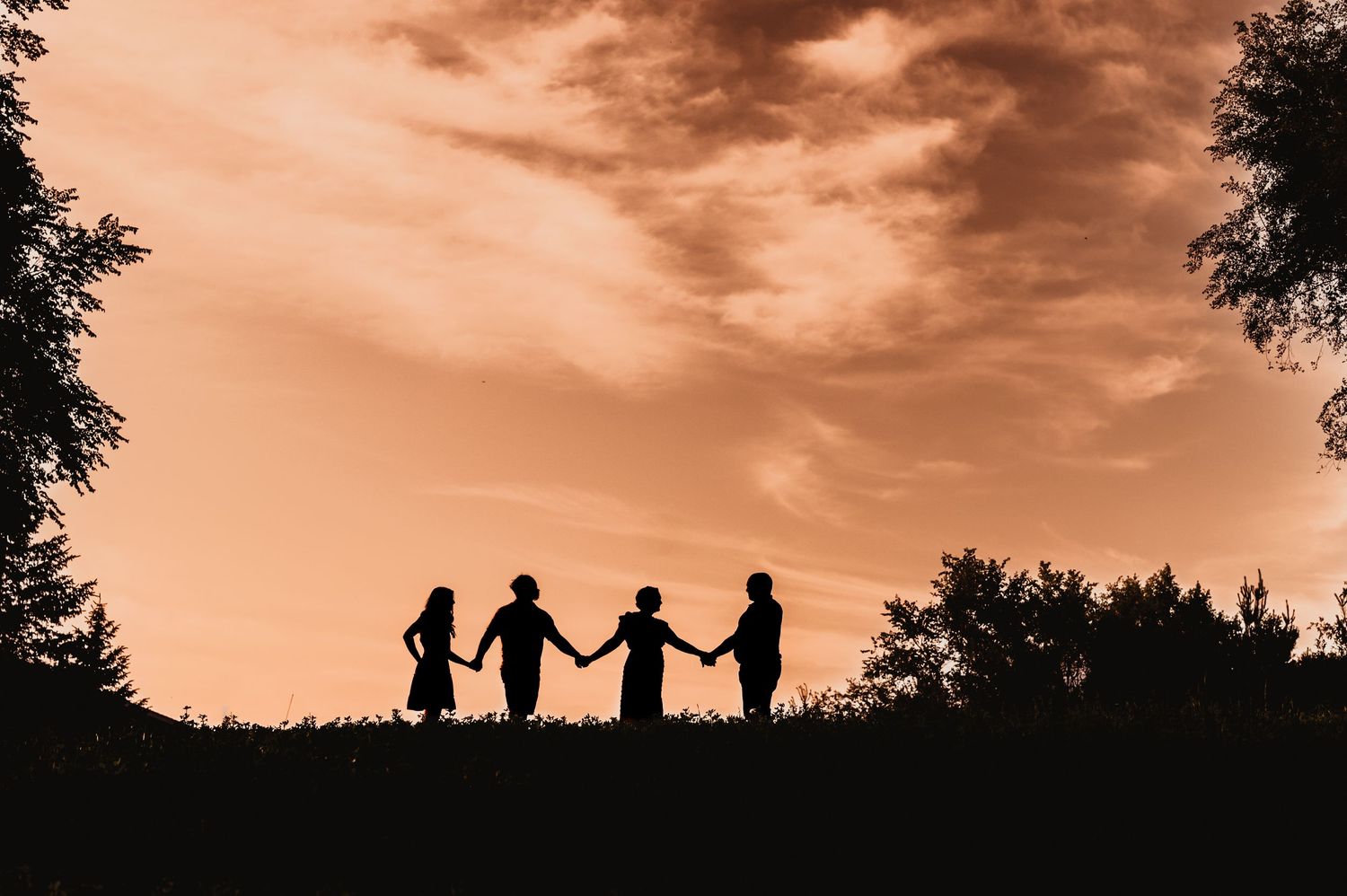 Silhouettes of four people holding hands against a sunset sky.